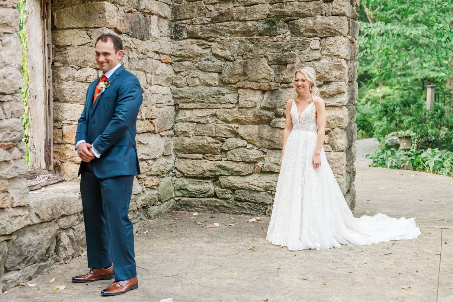 A wedding couple shares an intimate moment against a rustic stone wall backdrop in an outdoor setting.