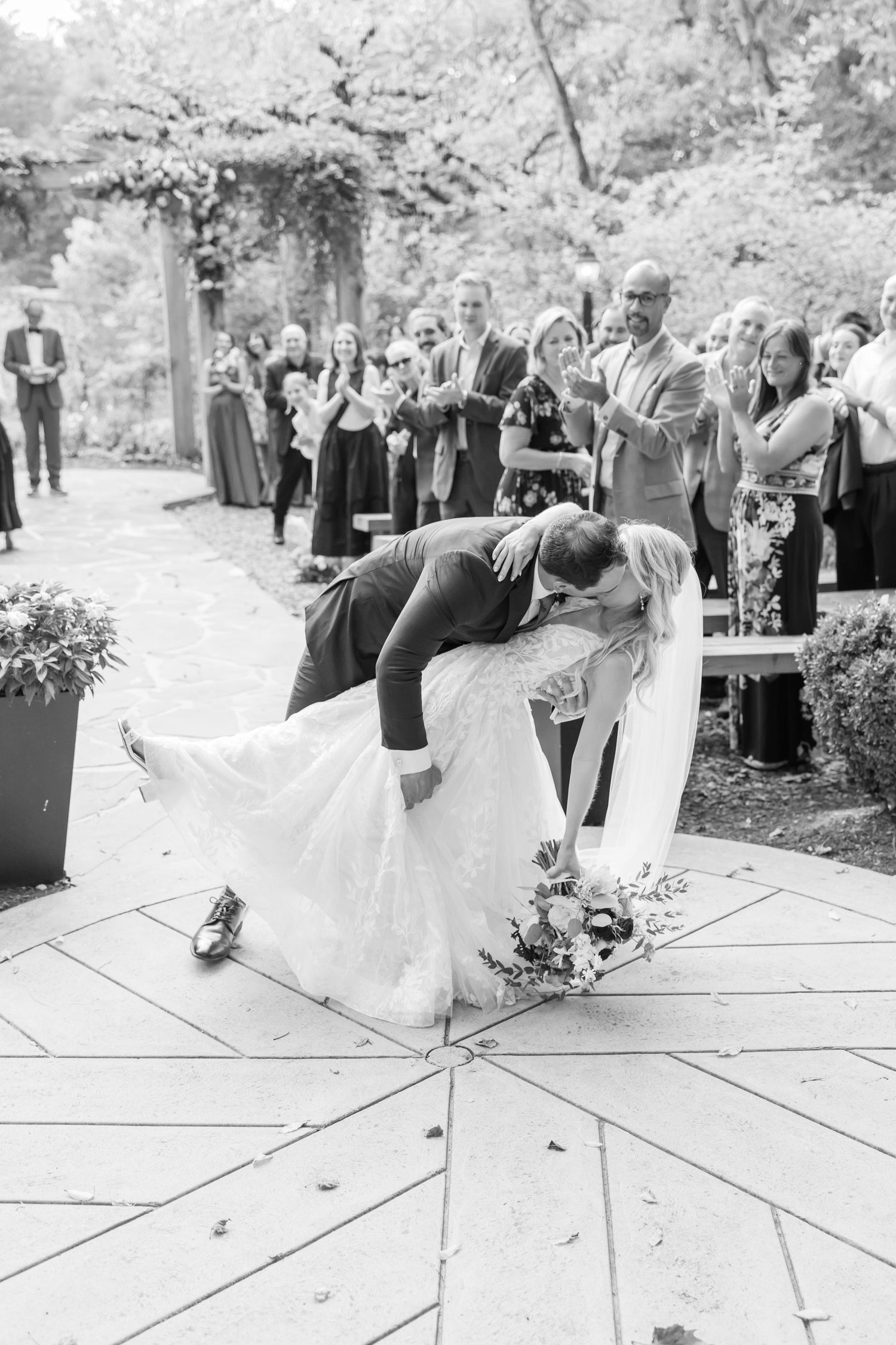A romantic wedding couple shares a dramatic dip kiss during their outdoor garden ceremony.