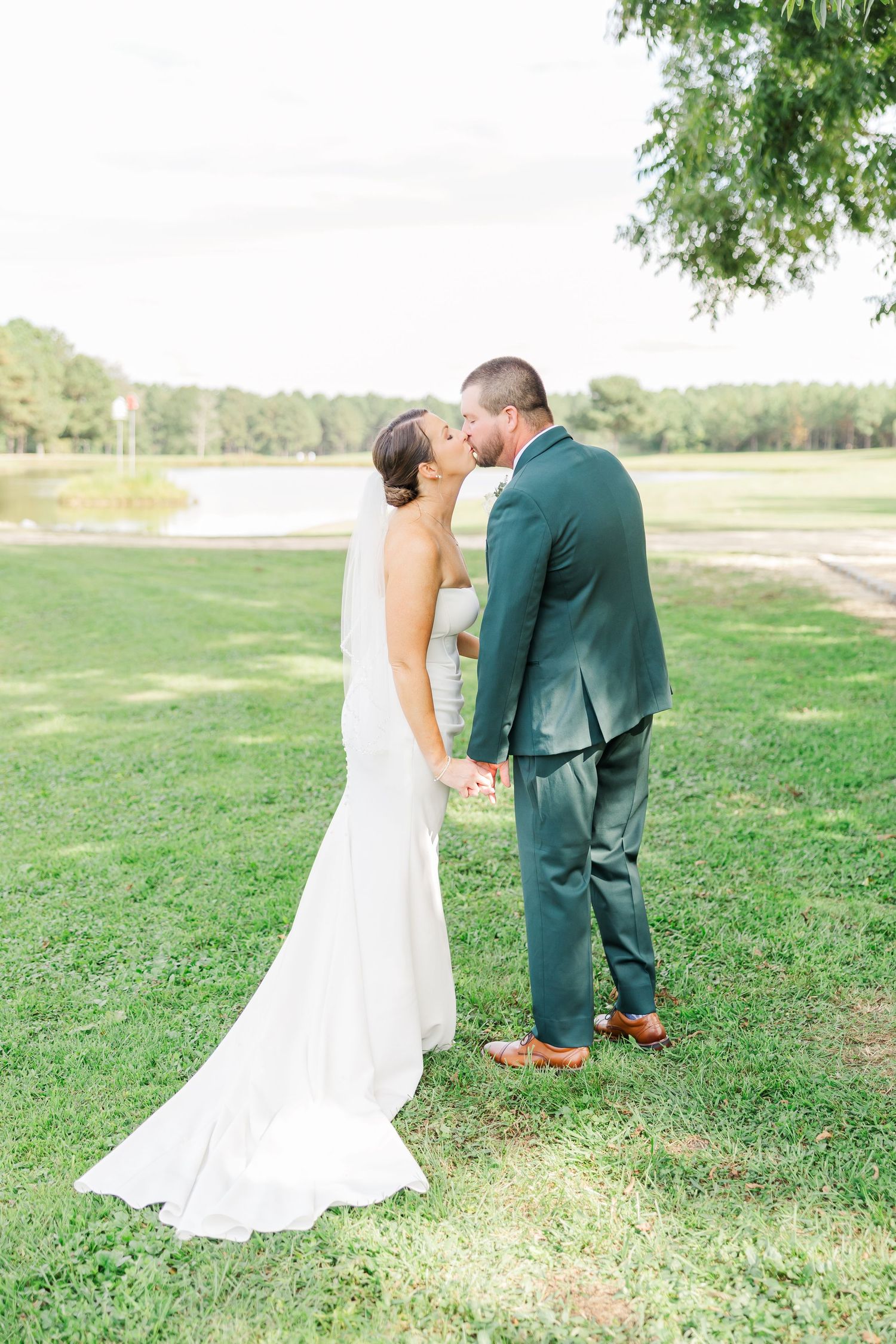A couple shares a romantic moment on a grassy lawn with a lake in the background during their wedding day.