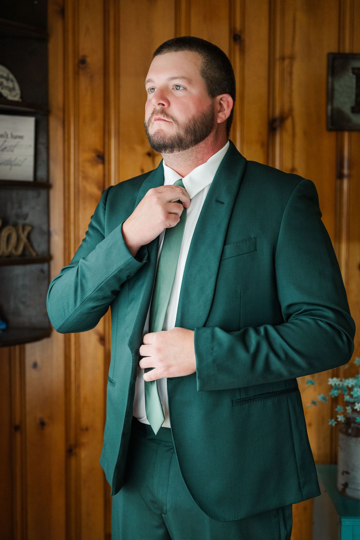 A series of photos showing someone adjusting a green suit jacket and white tie against a wood paneled wall.