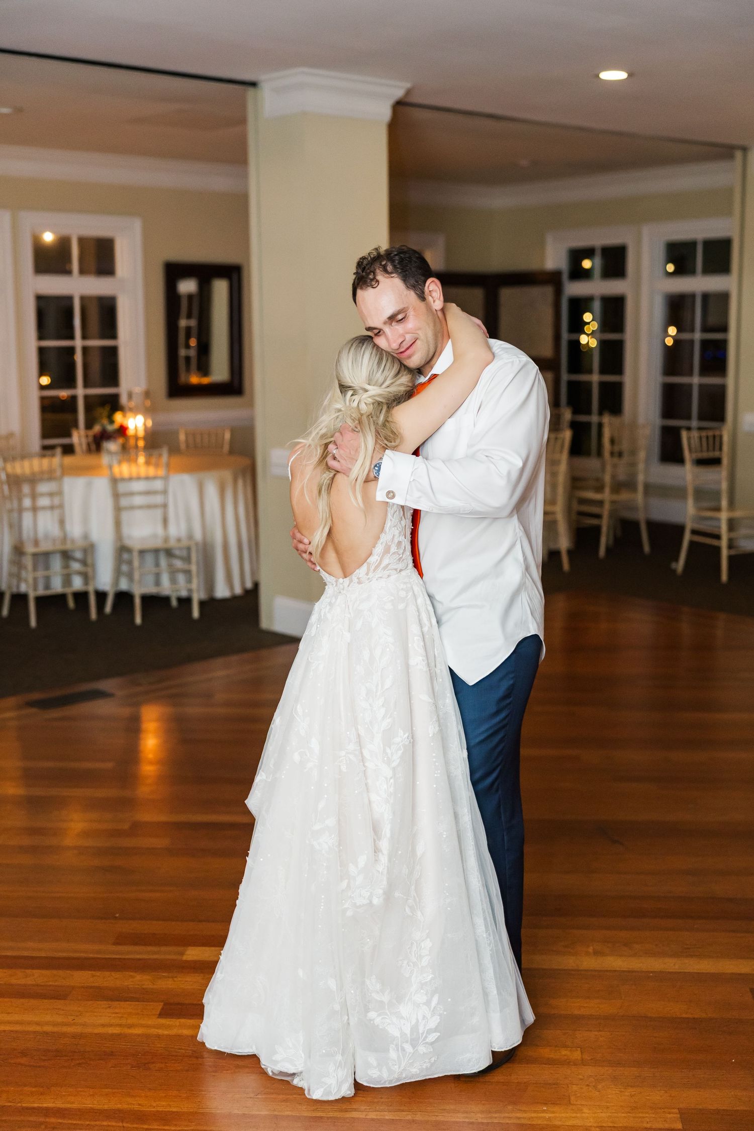 Romantic couple dances intimately in an elegant ballroom with wooden floors and white decor.