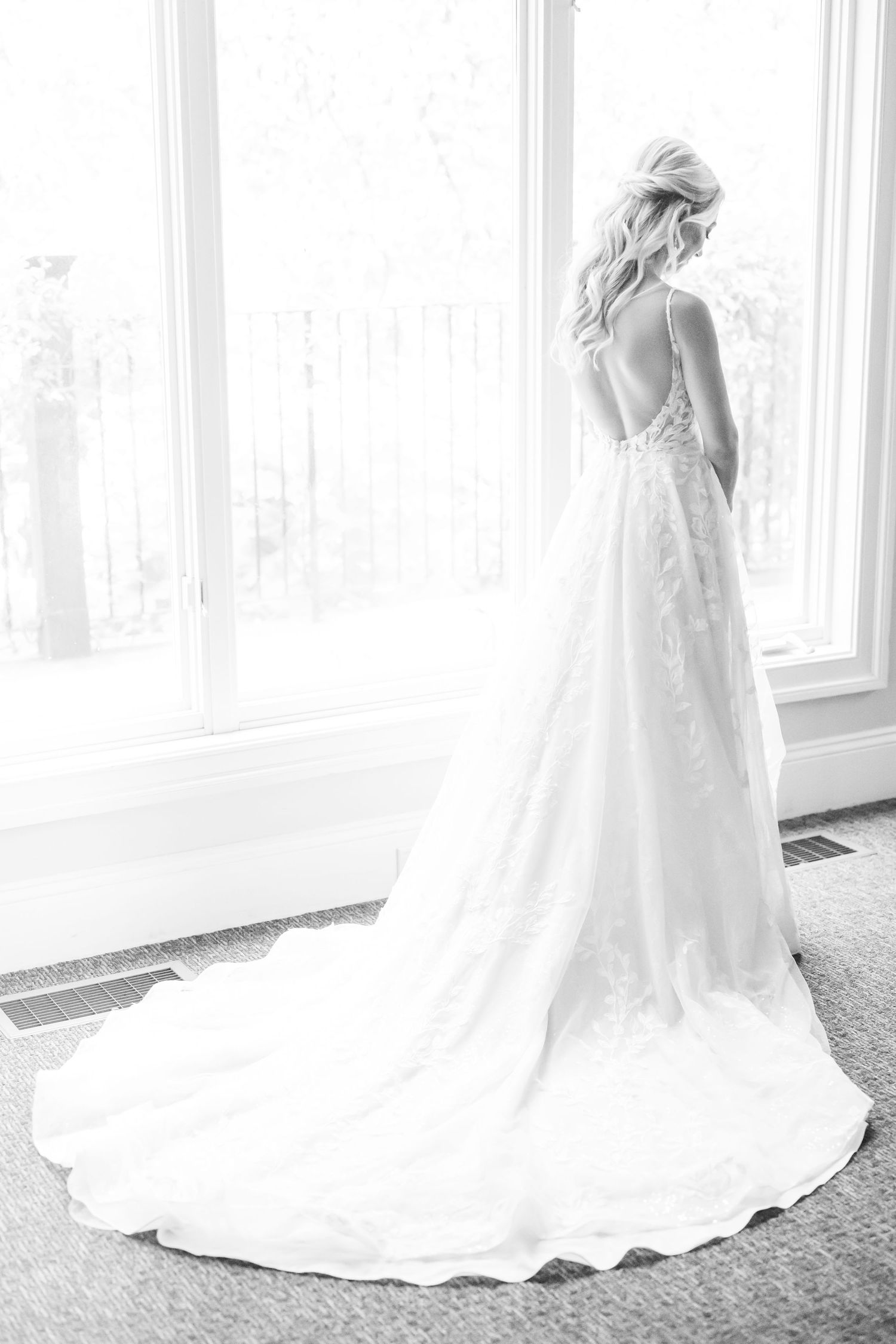 A bride in a flowing white wedding gown stands elegantly by large windows in a series of connected photos.
