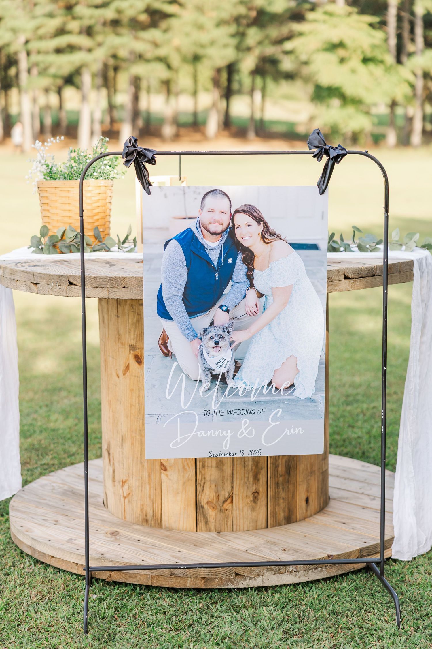 Wooden circular platform decorated with white fabric and photo displays in an outdoor wedding setting.