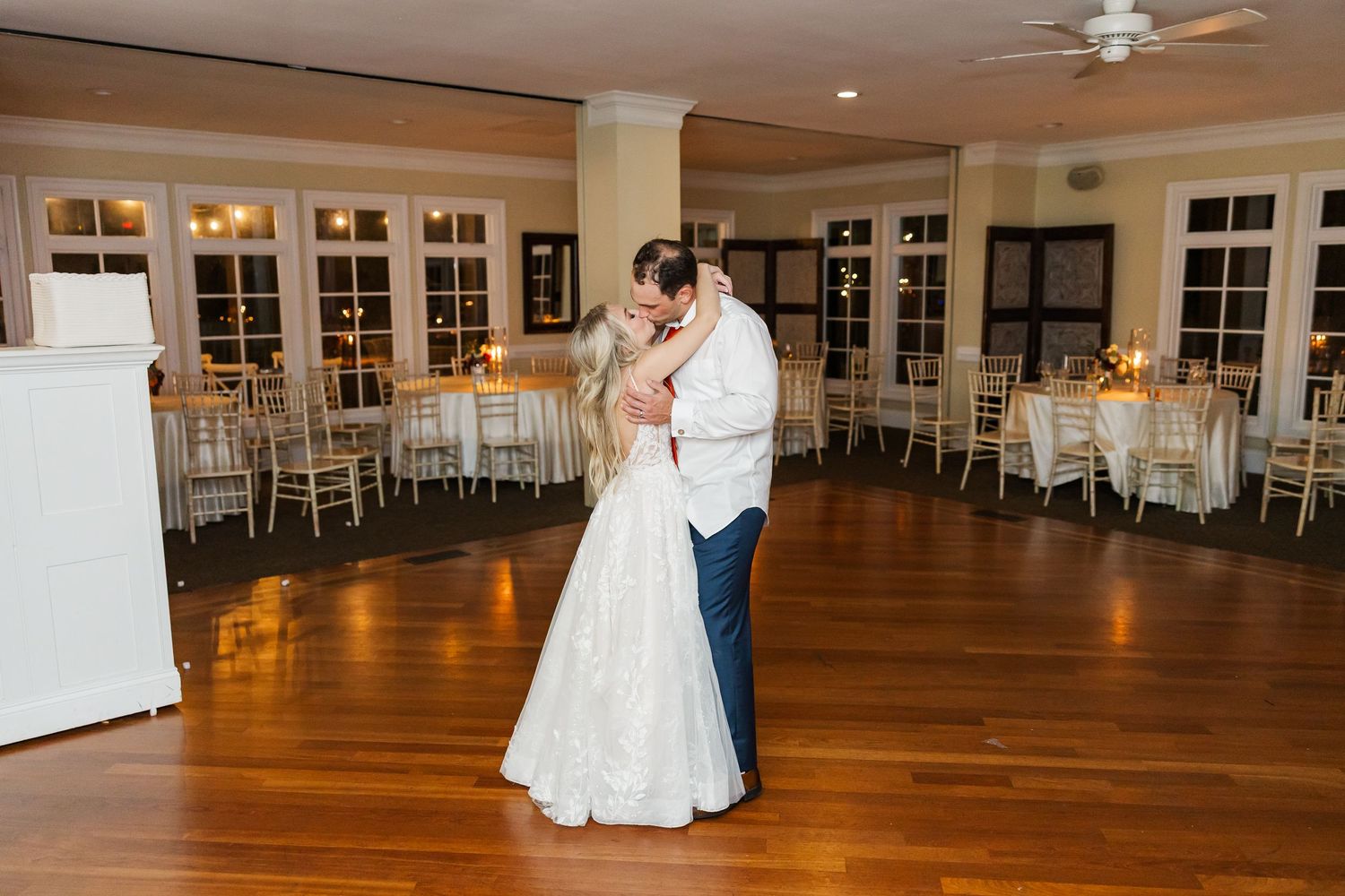 Couple dancing in an elegant ballroom with hardwood floors and white decor.