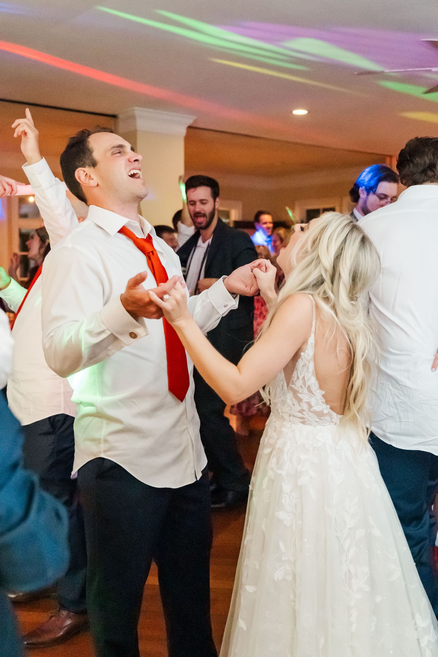 Wedding reception dance party with colorful disco lights illuminating guests dancing and celebrating on the dance floor.