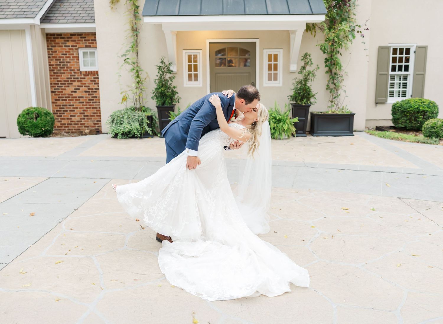 Wedding couple spinning and embracing on a light concrete courtyard in front of a classic white church entrance.