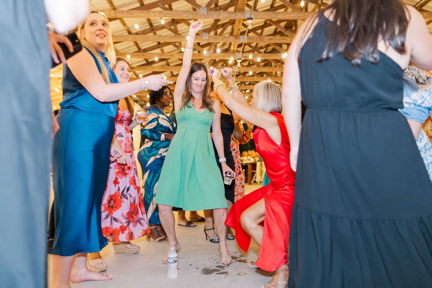 Women in colorful dresses dancing joyfully at an indoor wedding reception celebration.