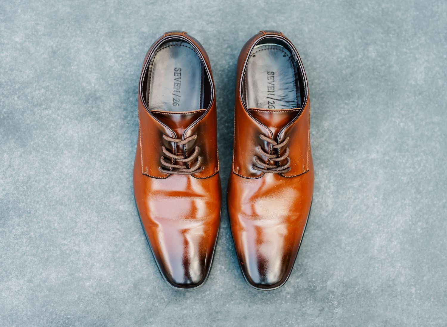 Collection of brown leather dress shoes arranged in a row on a gray textured background.
