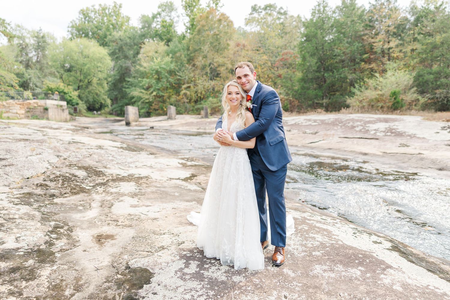 A tender moment between newlyweds standing on rocky terrain in classic wedding attire.