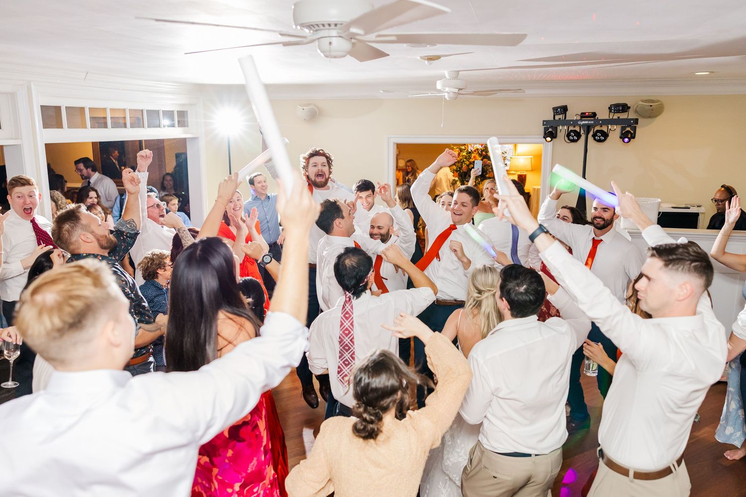 Wedding guests dancing and celebrating on a dance floor with their hands raised during a reception party.