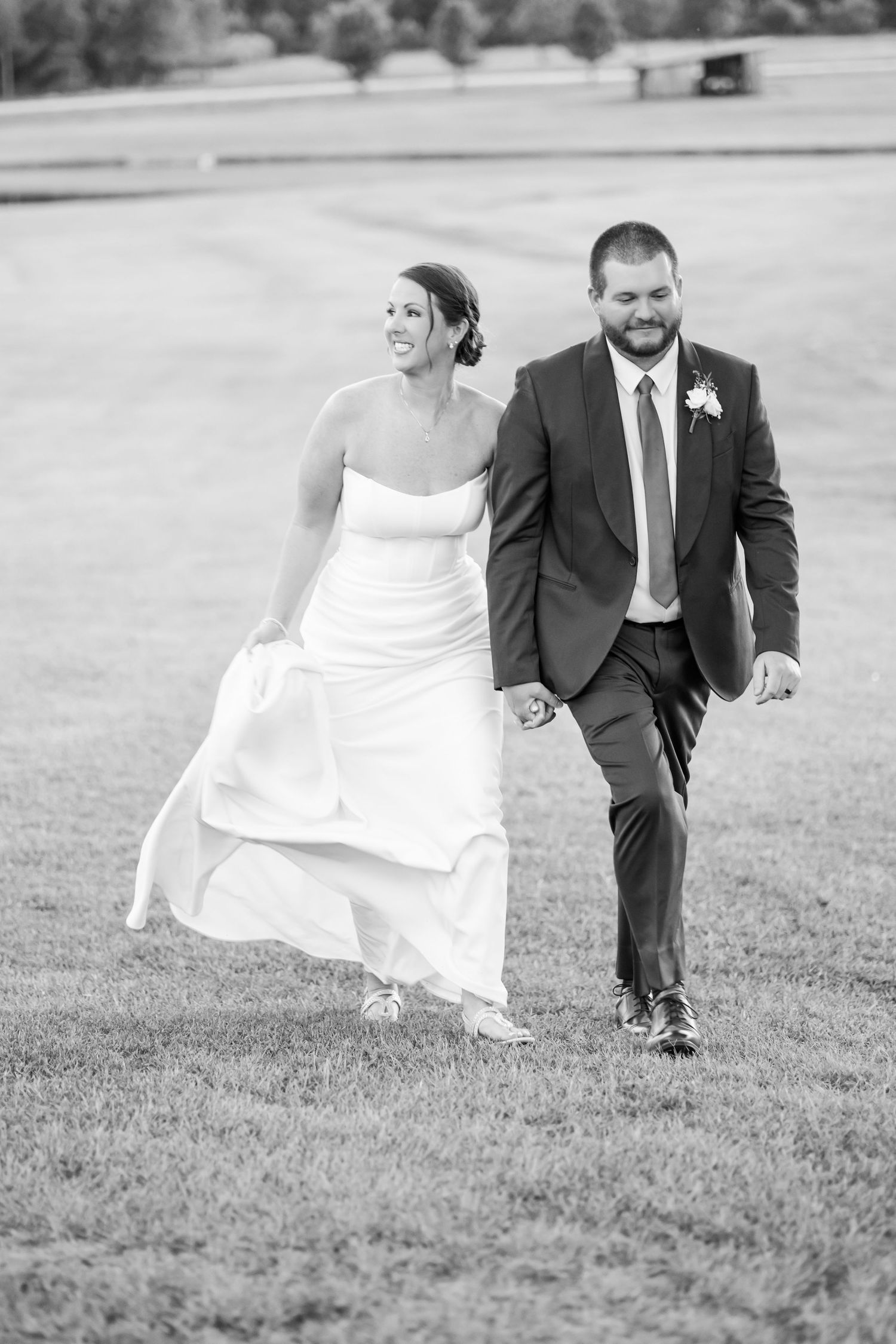 A black and white photo series of a couple running playfully across a grassy field in wedding attire.