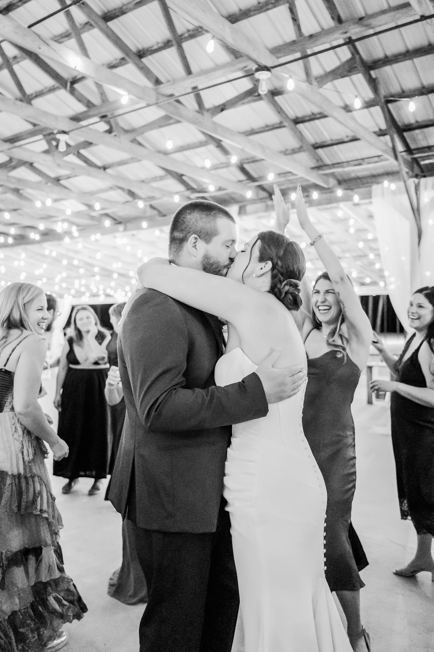 Bride and groom share a kiss on the dance floor surrounded by celebrating guests at their reception.