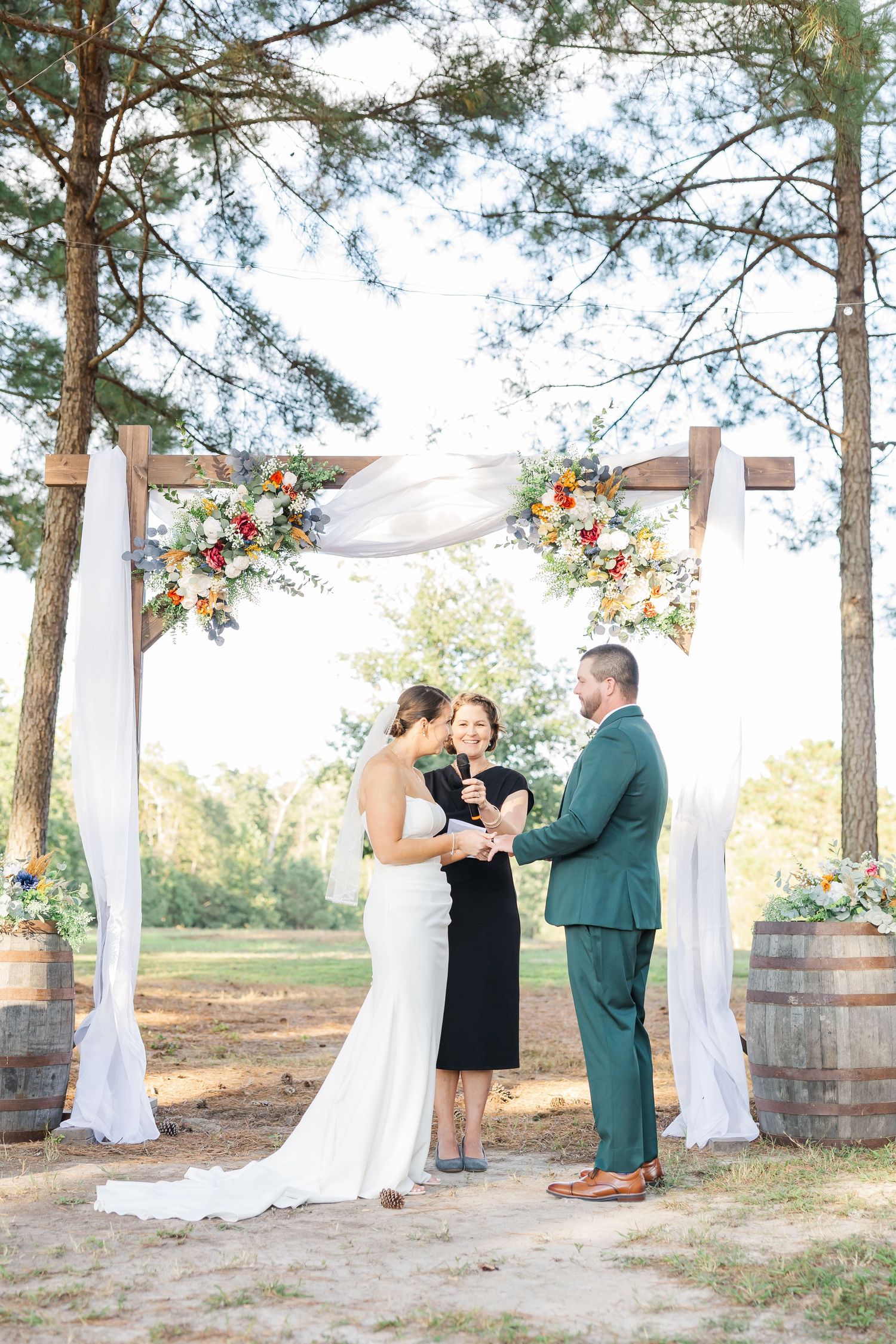 Couple exchanging vows under a rustic wooden arch with colorful floral arrangements at an outdoor wedding ceremony.