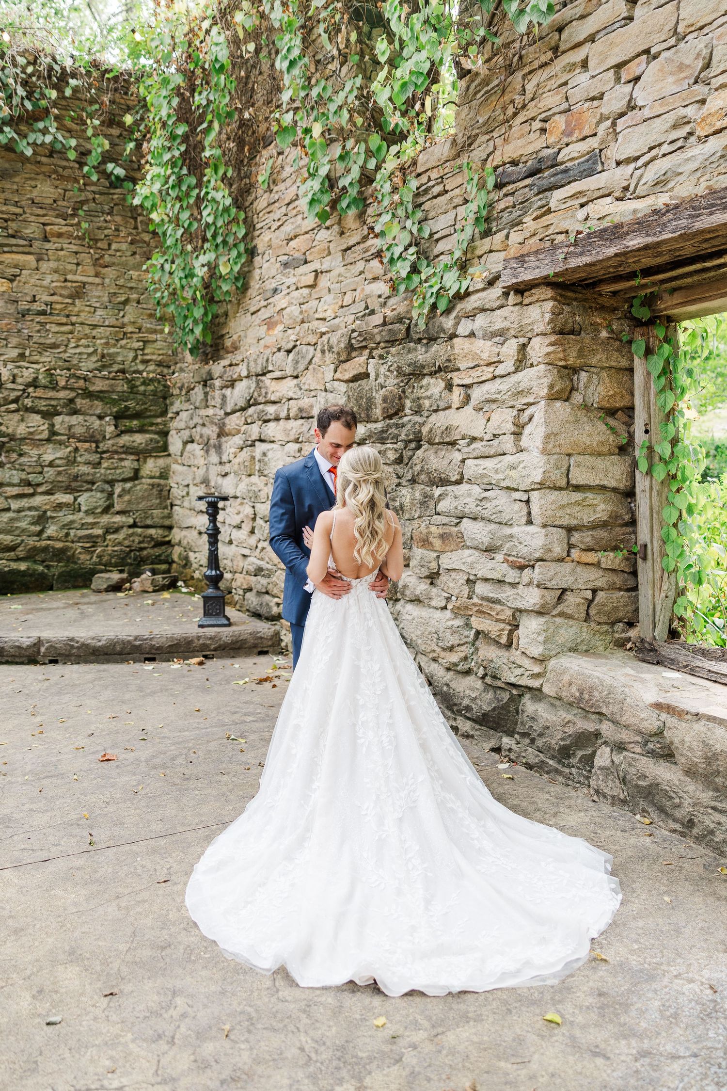 A wedding couple embraces and spins in a beautiful stone courtyard surrounded by greenery and natural light.