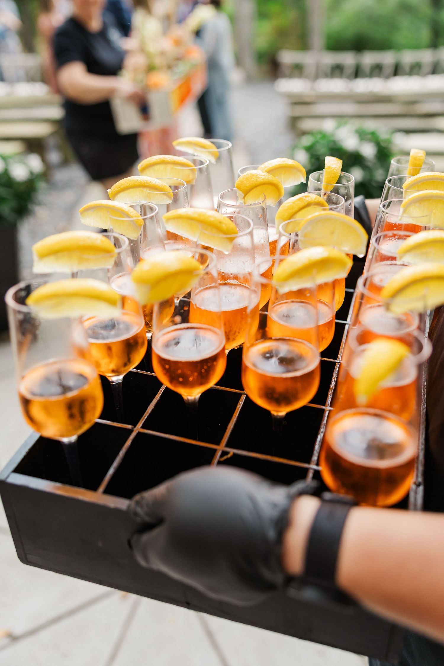 A row of elegant cocktails garnished with orange slices lined up on a black serving tray at an event.
