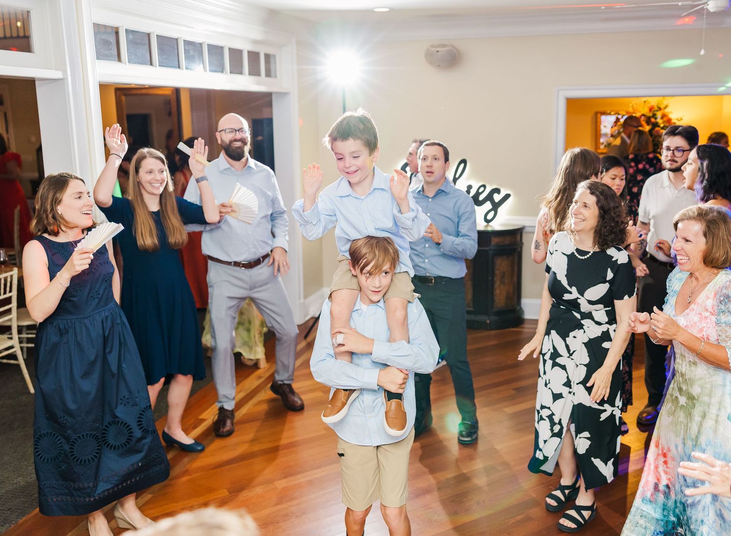 Wedding guests dancing together on a wooden dance floor during a lively reception celebration.