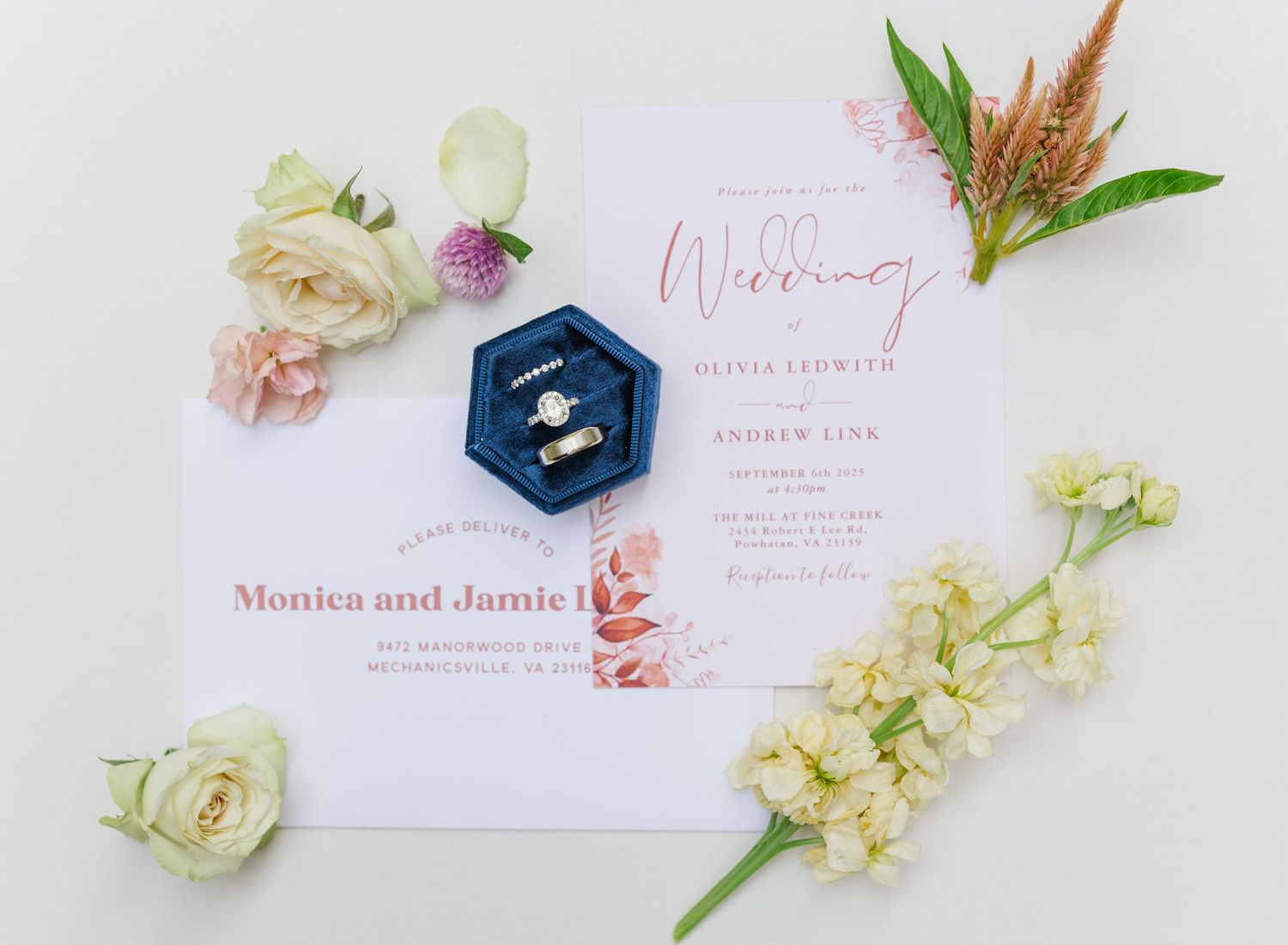 Wedding invitation suite with pink calligraphy, white roses, and decorative elements arranged on a light background.