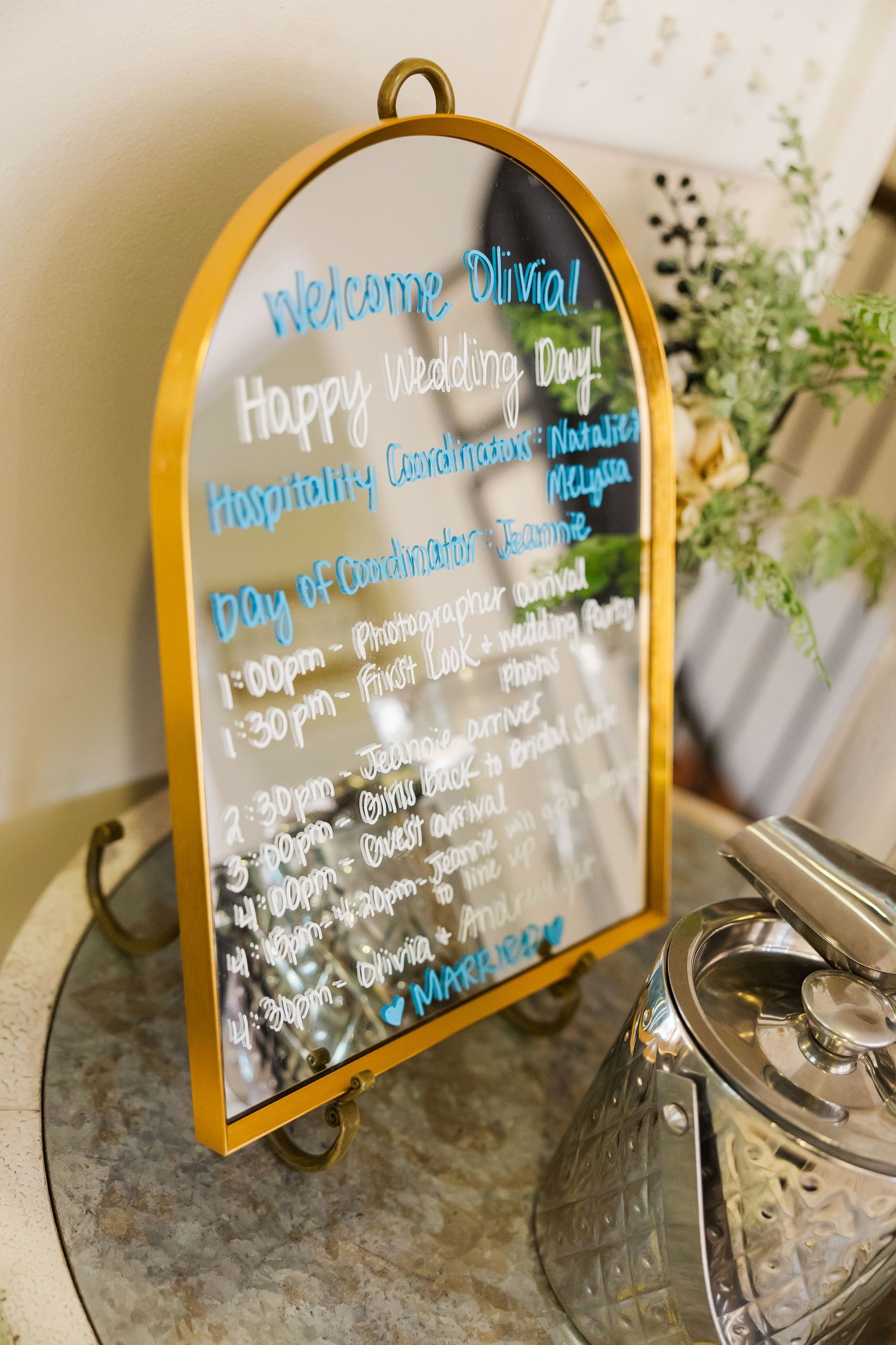 Gold-framed mirror signs display wedding day timeline and welcome messages in blue text.