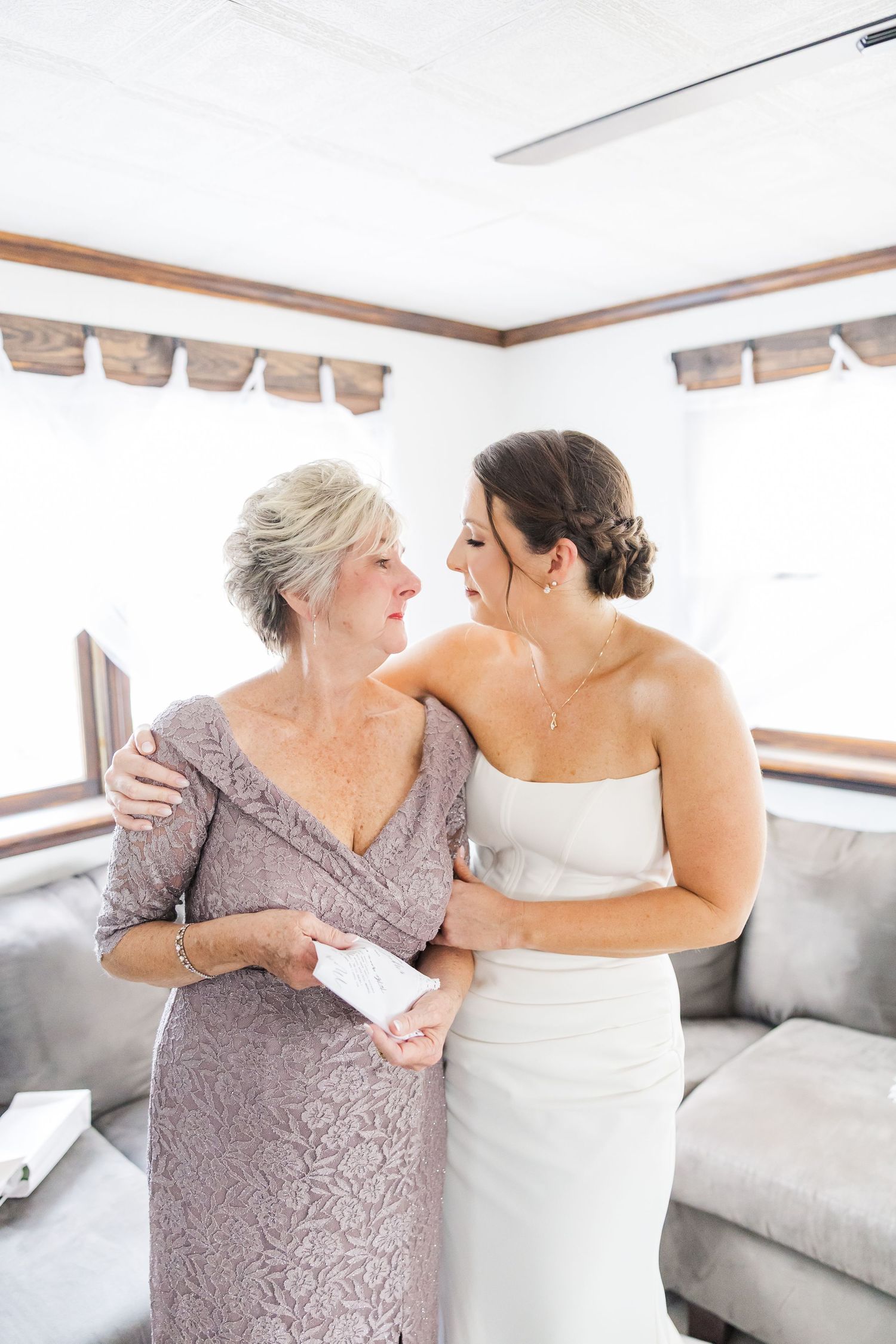 Two people in formal attire sharing an emotional moment in a room with white walls and grey furniture.