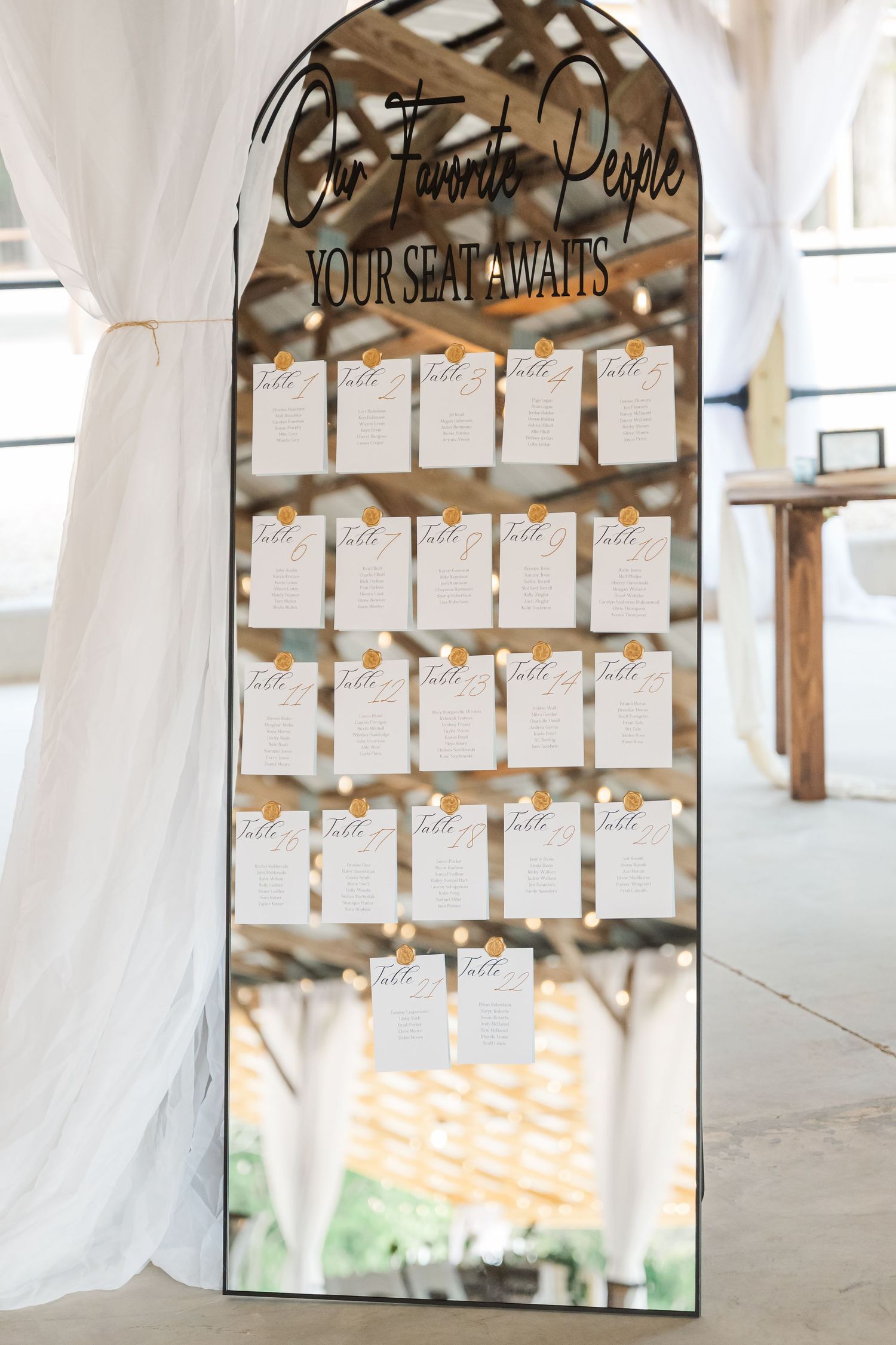Arched mirror seating chart display reading Our Favorite People Your Seat Awaits with gold-pinned table assignment cards.