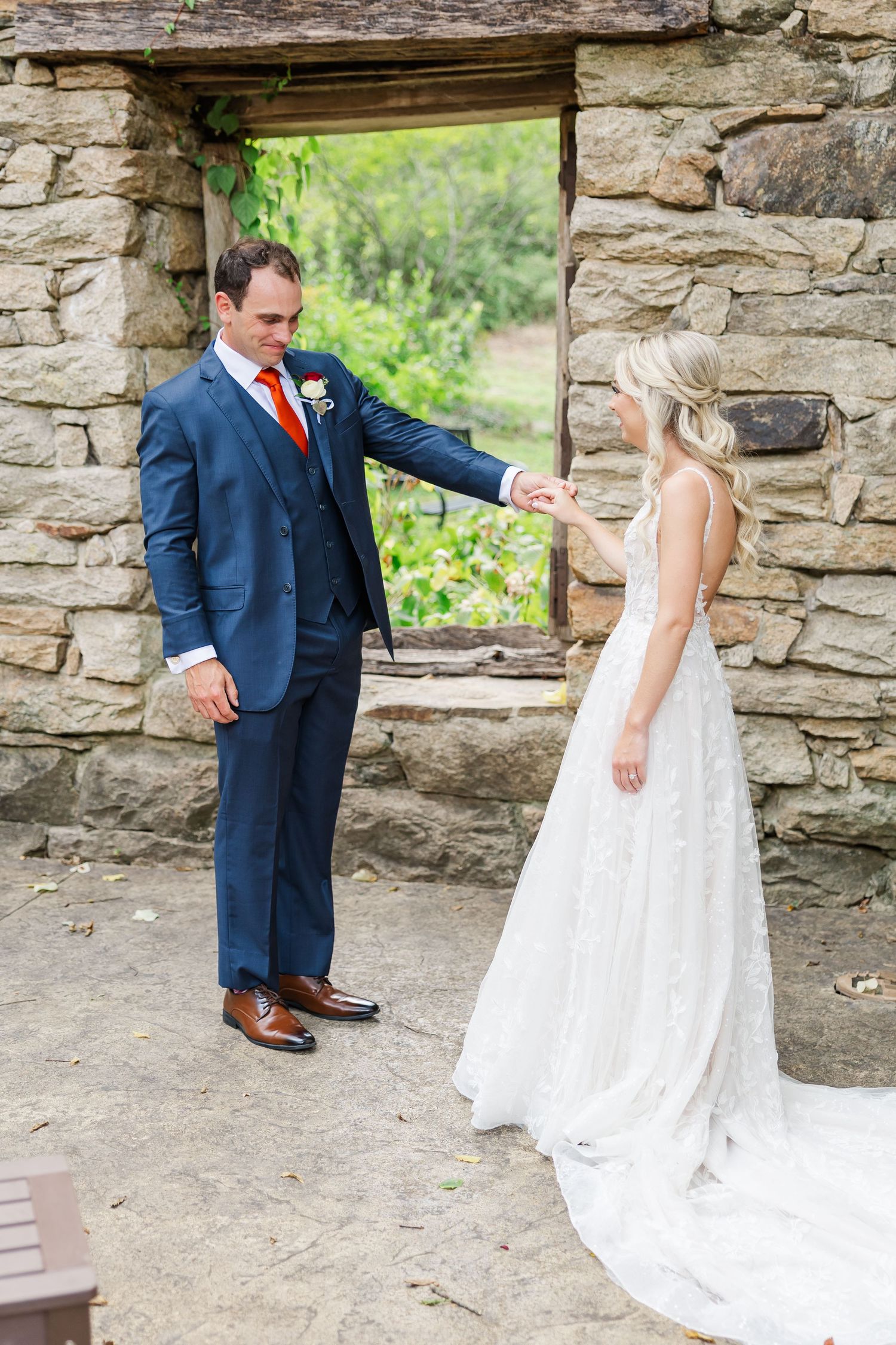 A couple shares a romantic moment in front of a rustic stone wall with a window opening at their wedding.