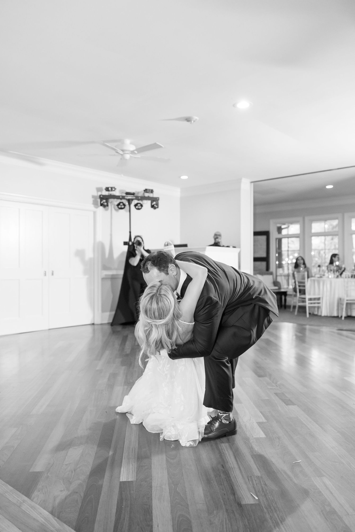 Black and white sequence showing a couple in wedding attire performing a playful dance dip on a wooden floor.