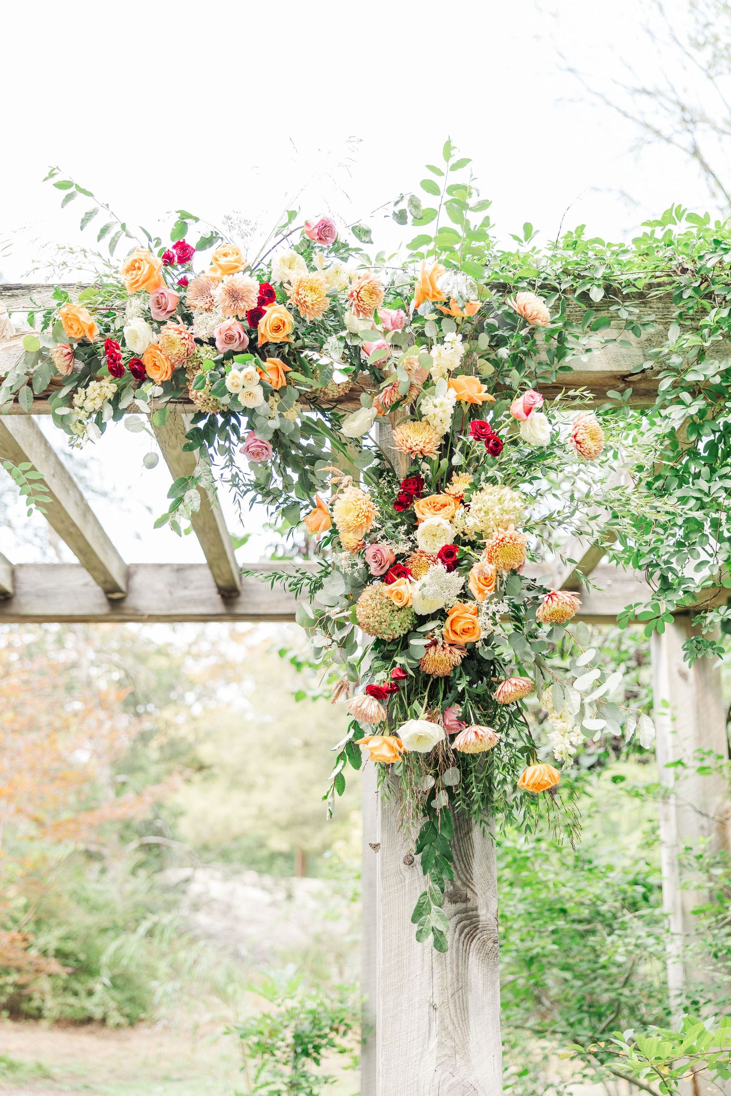 A wooden pergola decorated with vibrant orange and red flowers and greenery creates a romantic garden archway.