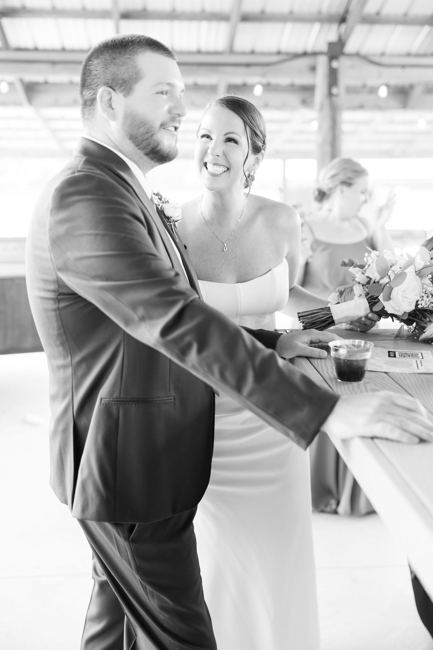 Black and white photo of a smiling bride and groom at their wedding reception standing together at a table.