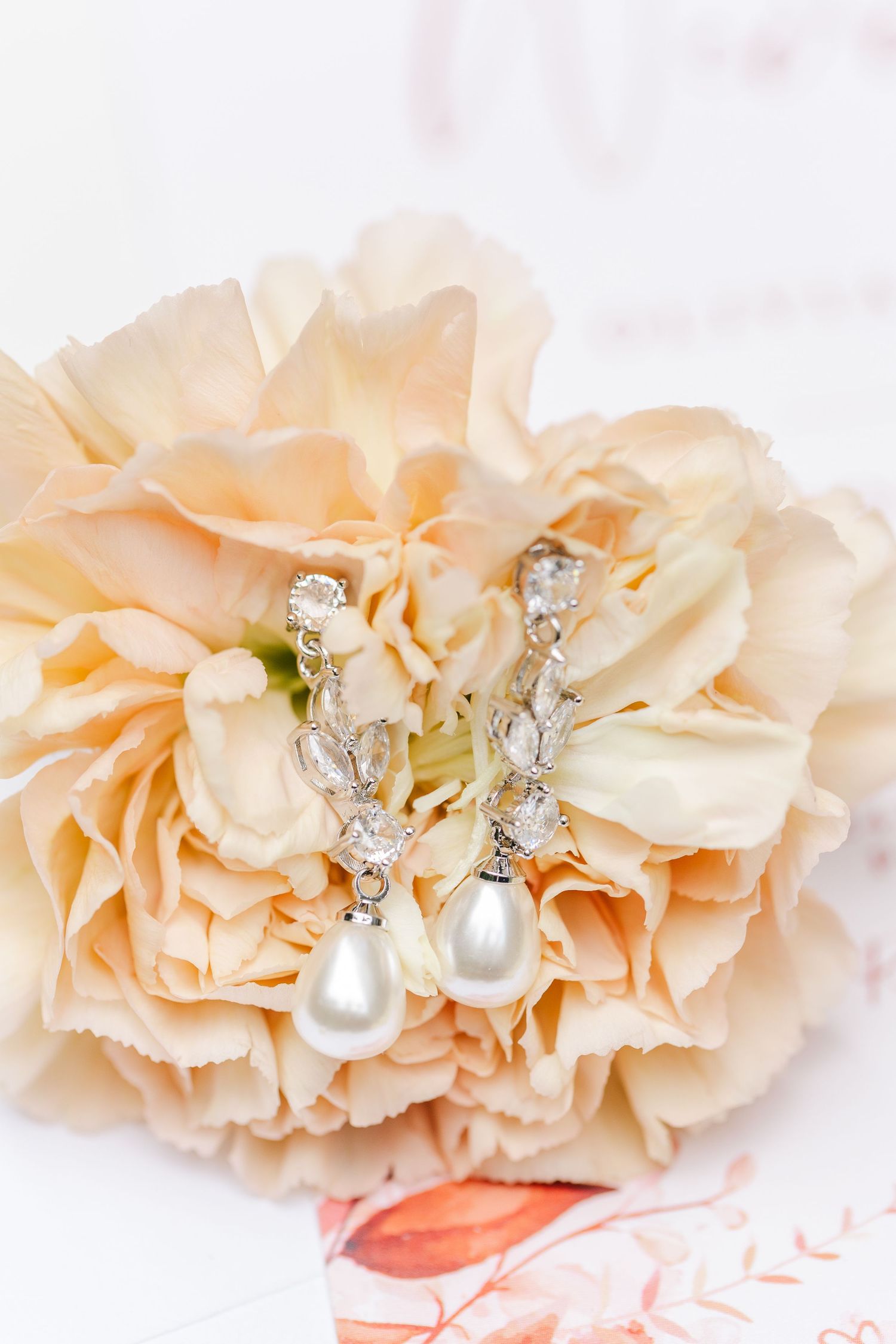 Delicate peach roses adorned with pearl and crystal jewelry decorations on a soft pink background.
