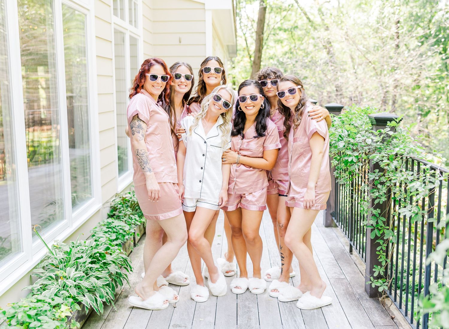 A group wearing matching pink satin robes poses together on a sunny outdoor porch.