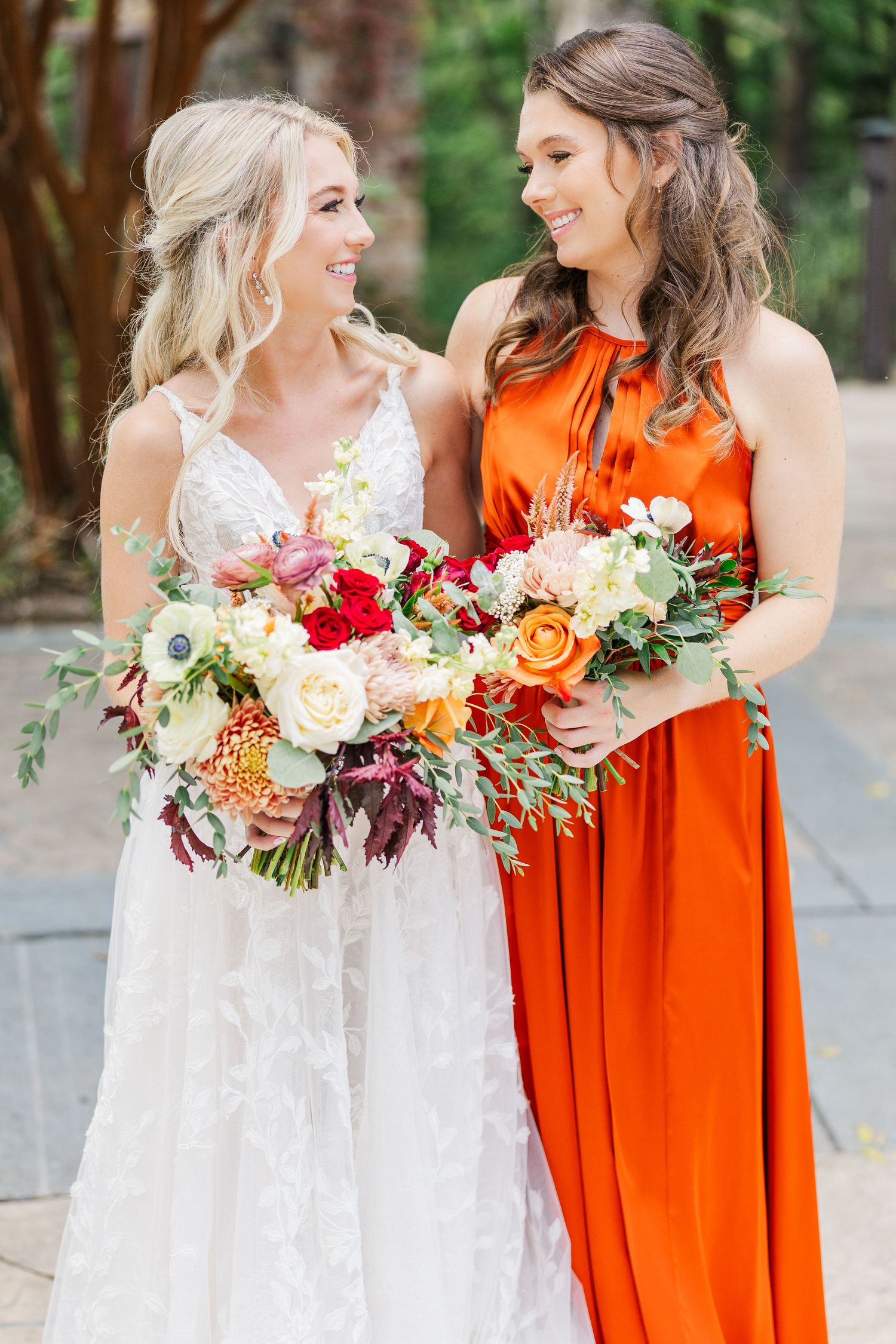 Close-up of wedding party members holding lush floral bouquets in white and orange attire.