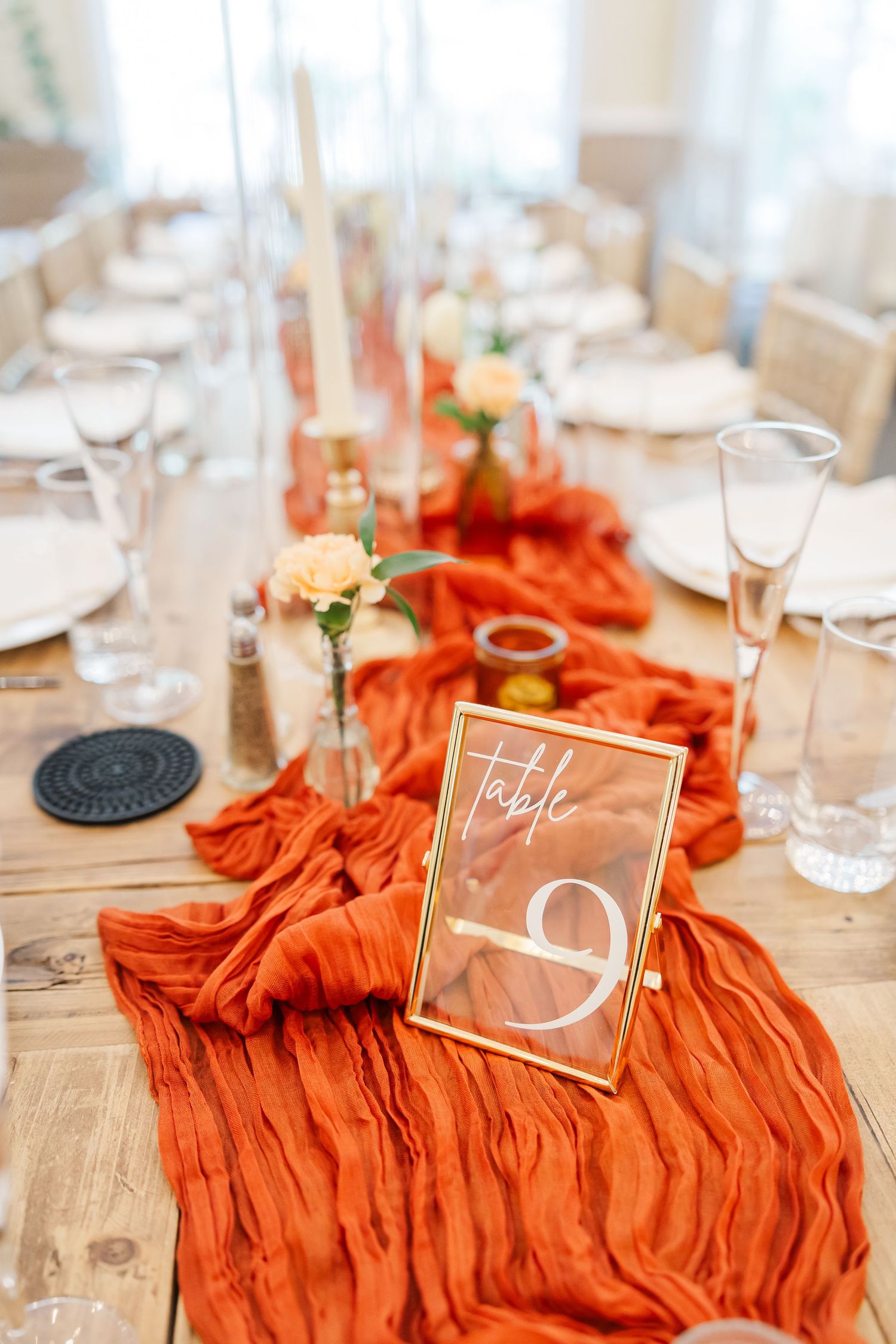 Wedding table settings with burnt orange runners and clear acrylic table numbers.