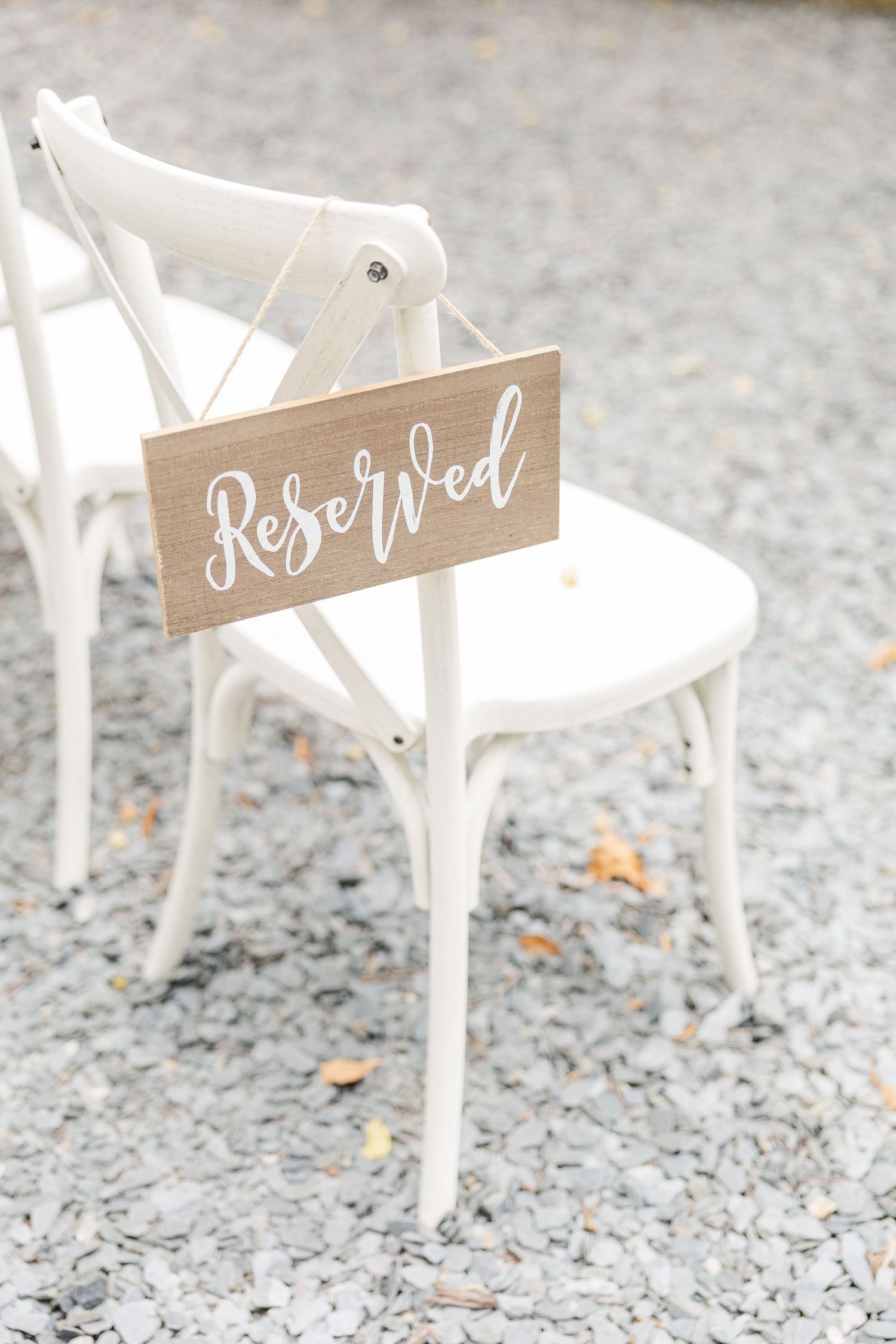White wooden chairs with rustic 'Reserved' signs at a wedding ceremony setup on a gravel surface.