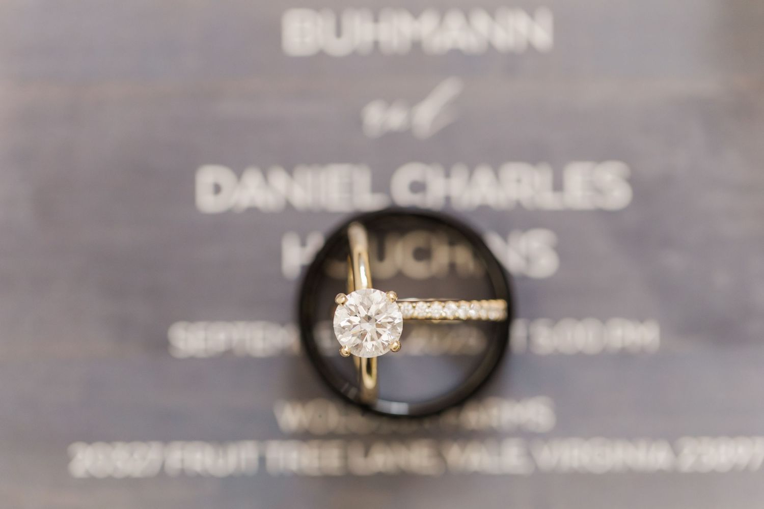 A collection of engagement rings and wedding bands displayed on a gray surface with jewelry brand names visible.