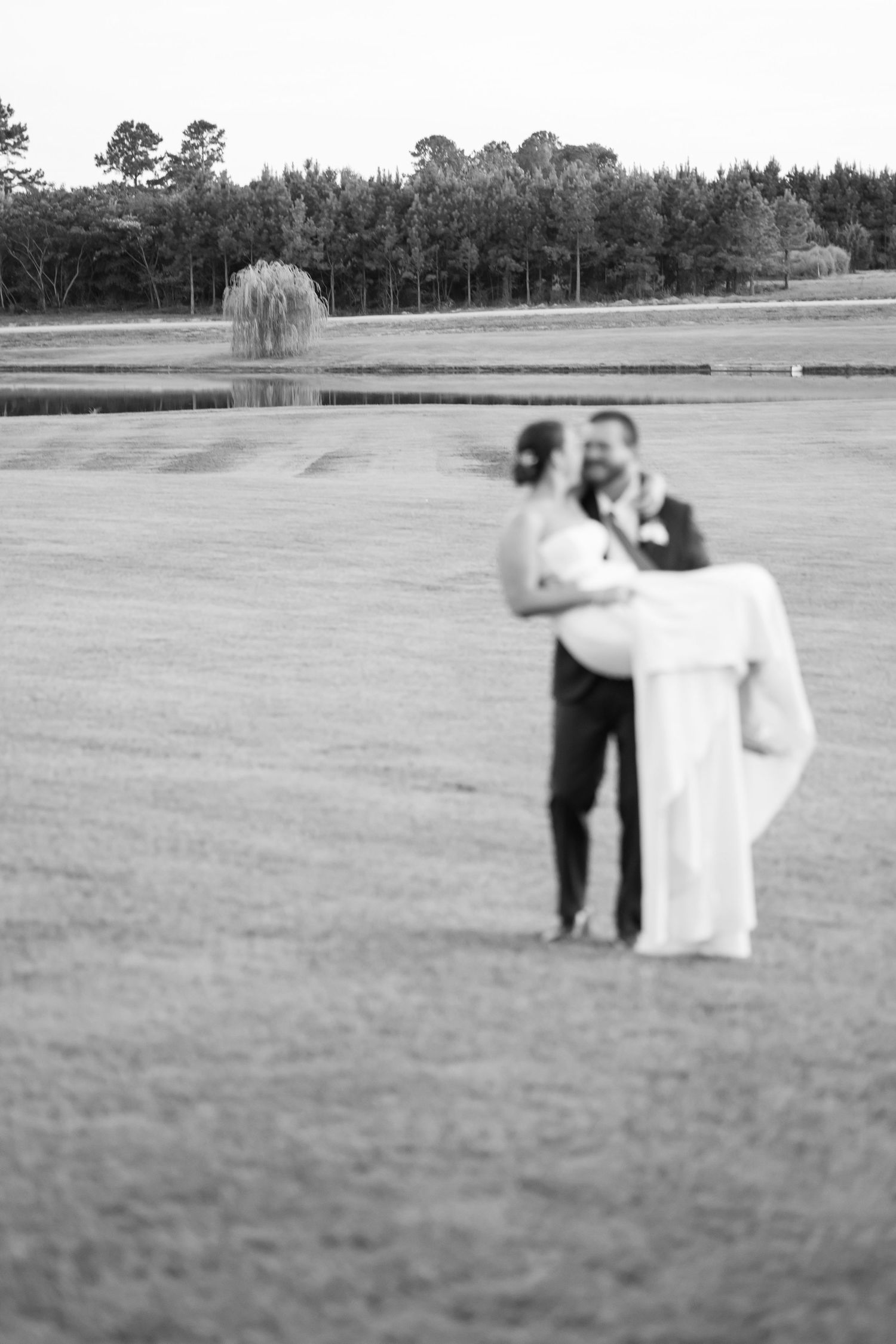 A couple dances together in an open field with trees in the background.