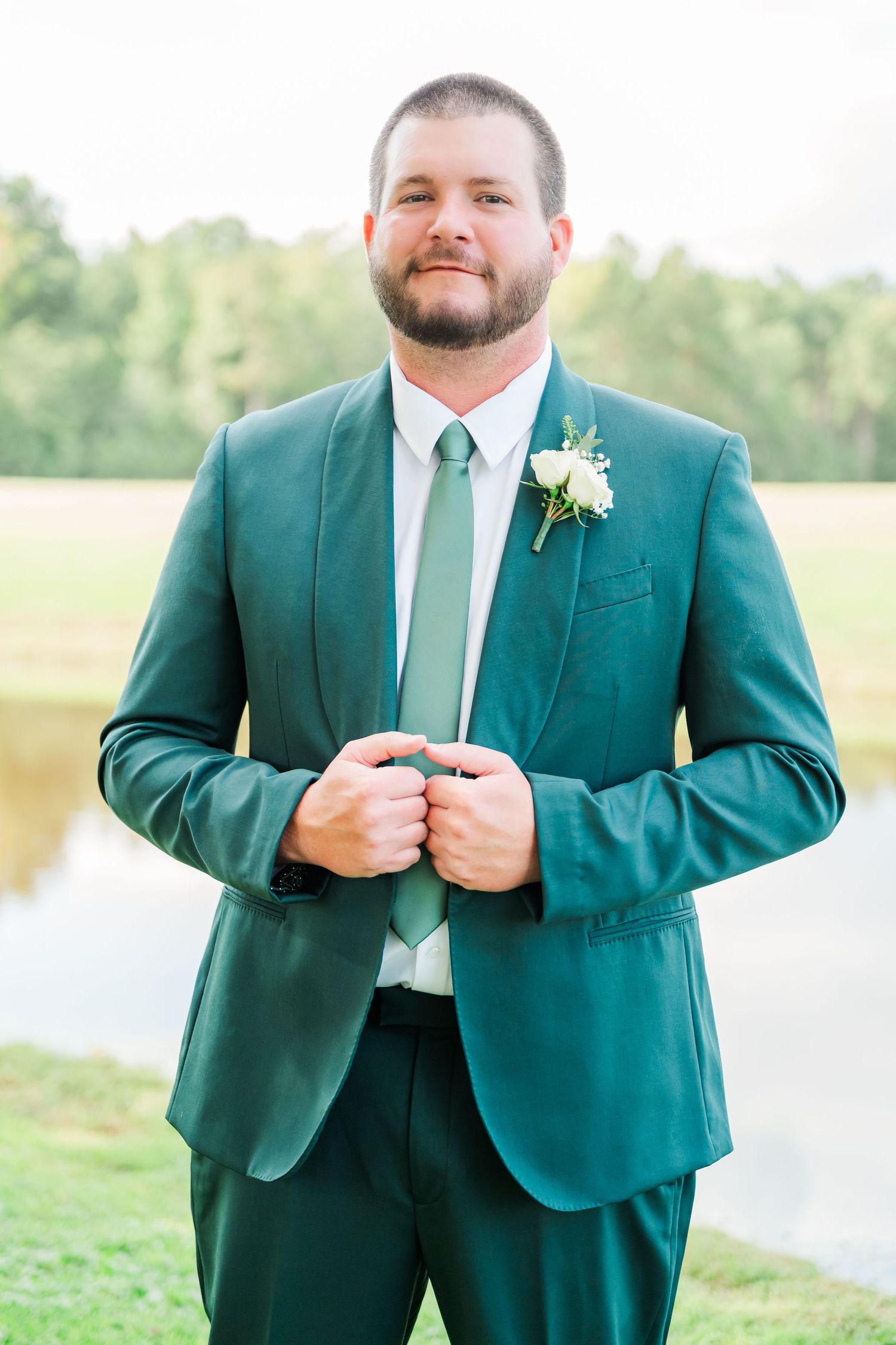 Close-up view of a groom in an emerald green suit adjusting his jacket buttons outdoors.