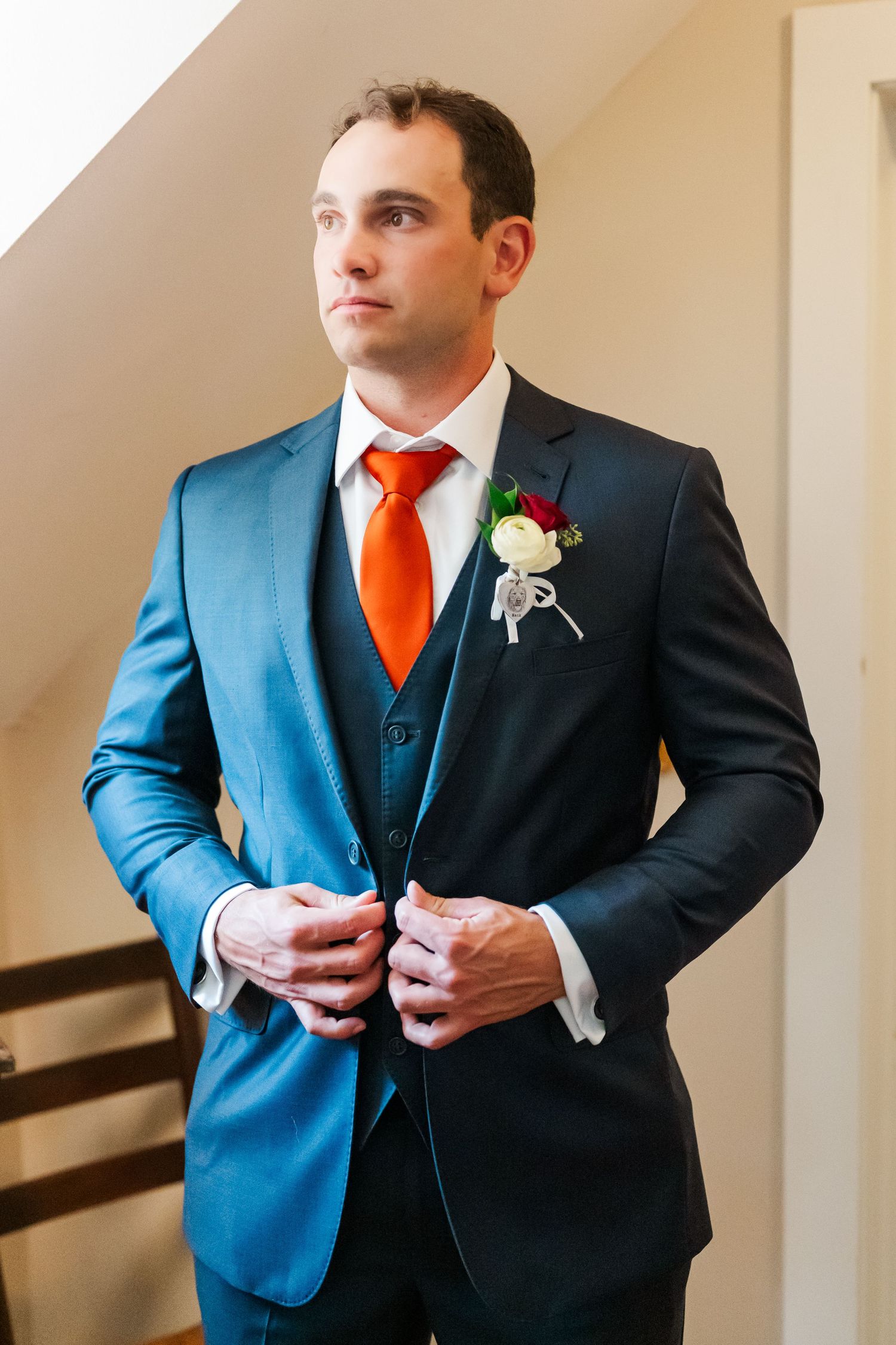 Groom adjusts tie wearing blue suit with orange accent in series of getting ready photos.