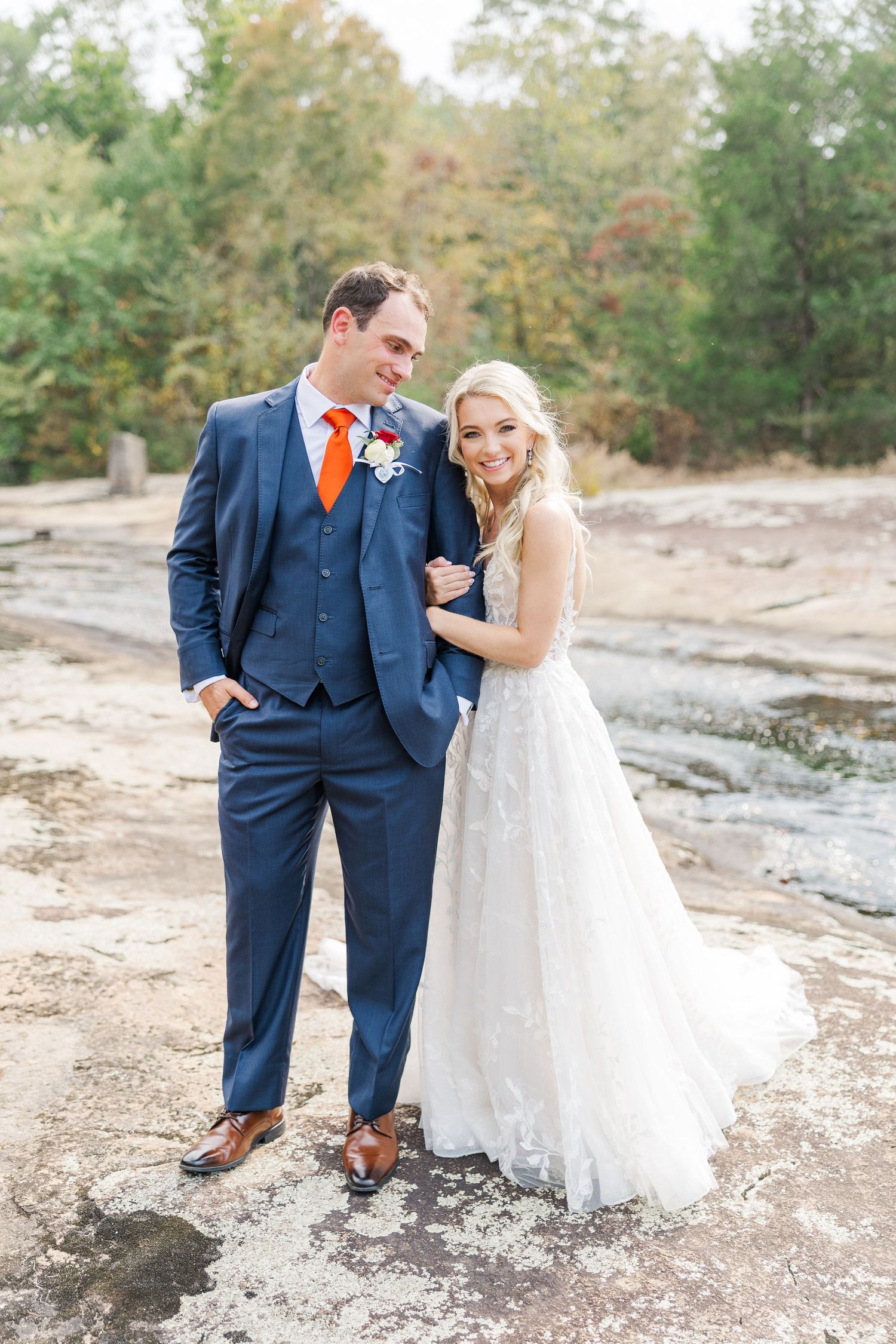 Wedding couple in navy suit and lace dress pose together on rocky outdoor terrain during autumn.