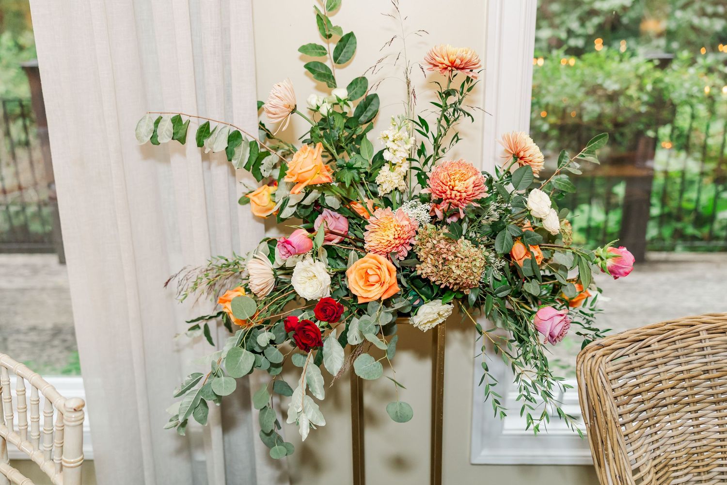 Elegant peach and coral floral arrangements with greenery decorate a wedding venue with white draping.