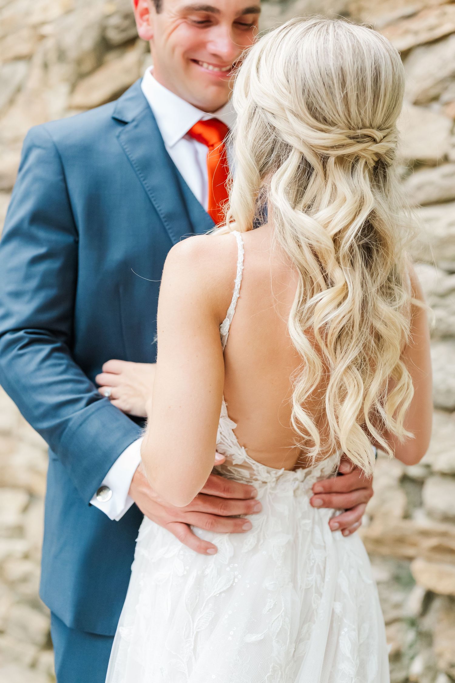 A romantic wedding moment showing a couple embracing, with the bride in white and groom in blue suit with orange tie.