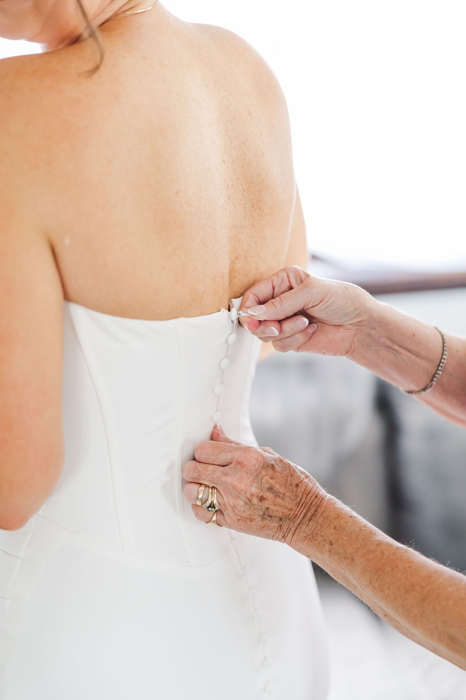 Hands adjusting the back of a white wedding dress with delicate lacing details.