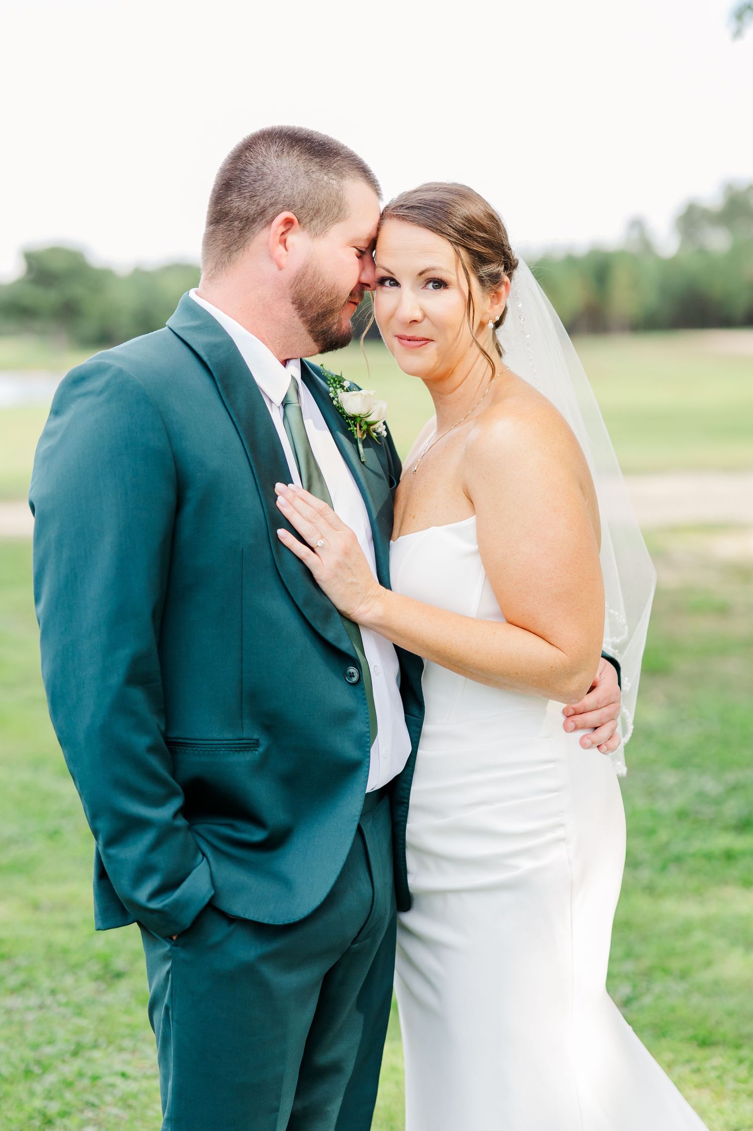 Romantic wedding couple embraces on a scenic golf course during golden hour.