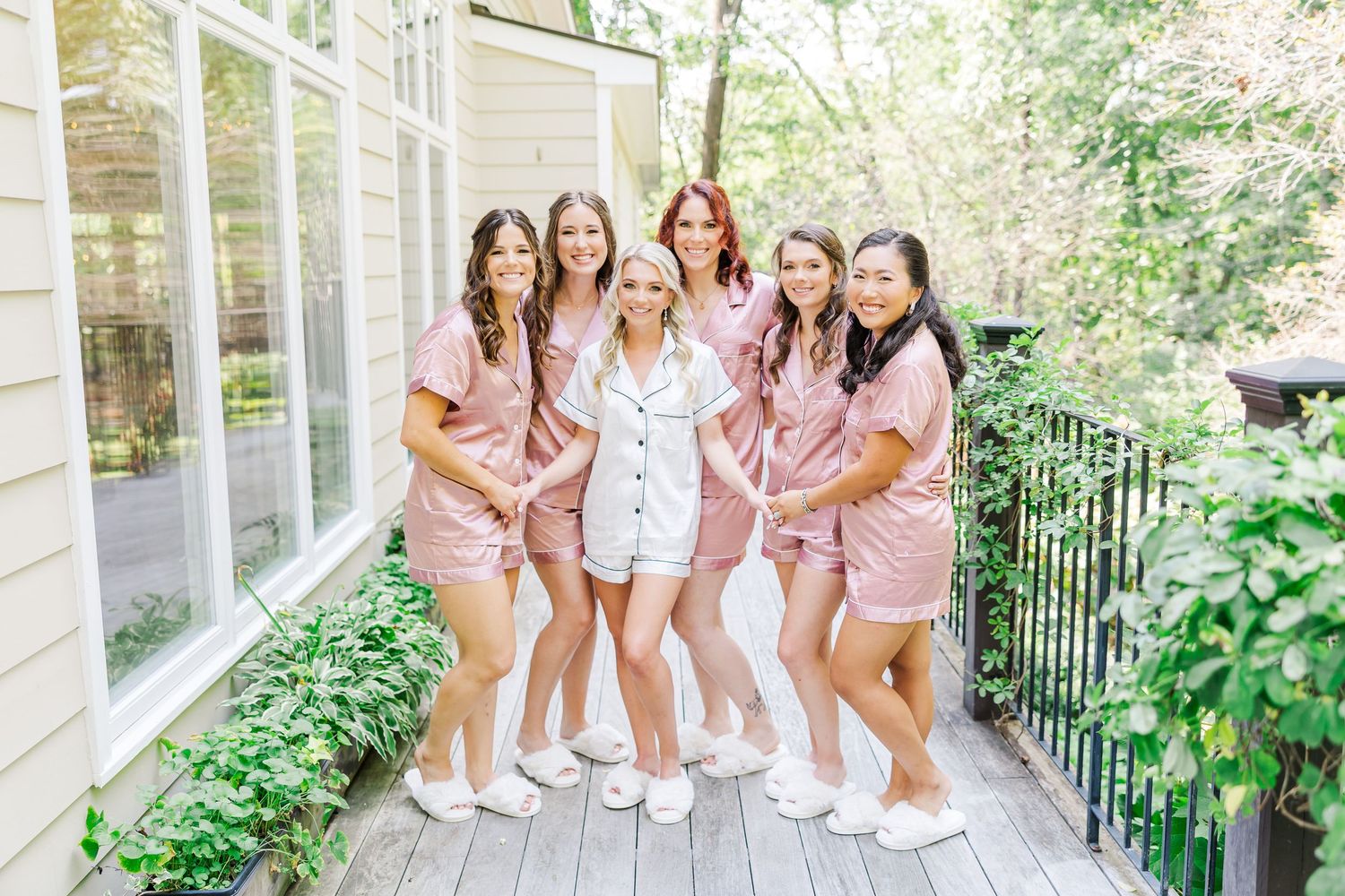 Group of bridesmaids in pink dresses posing together on a sunlit porch.