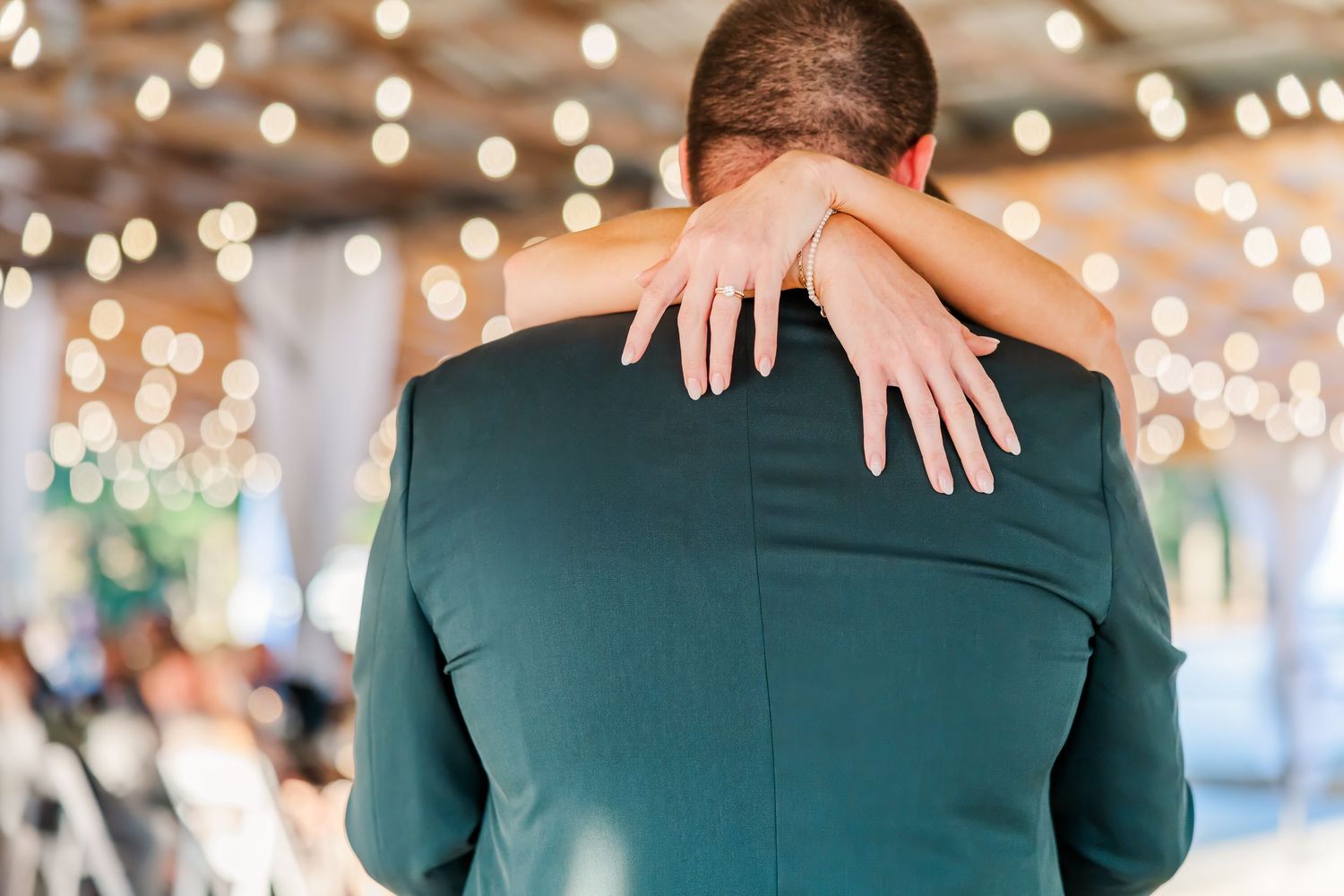 Bride wraps her arms around groom in green suit during first dance at wedding reception.