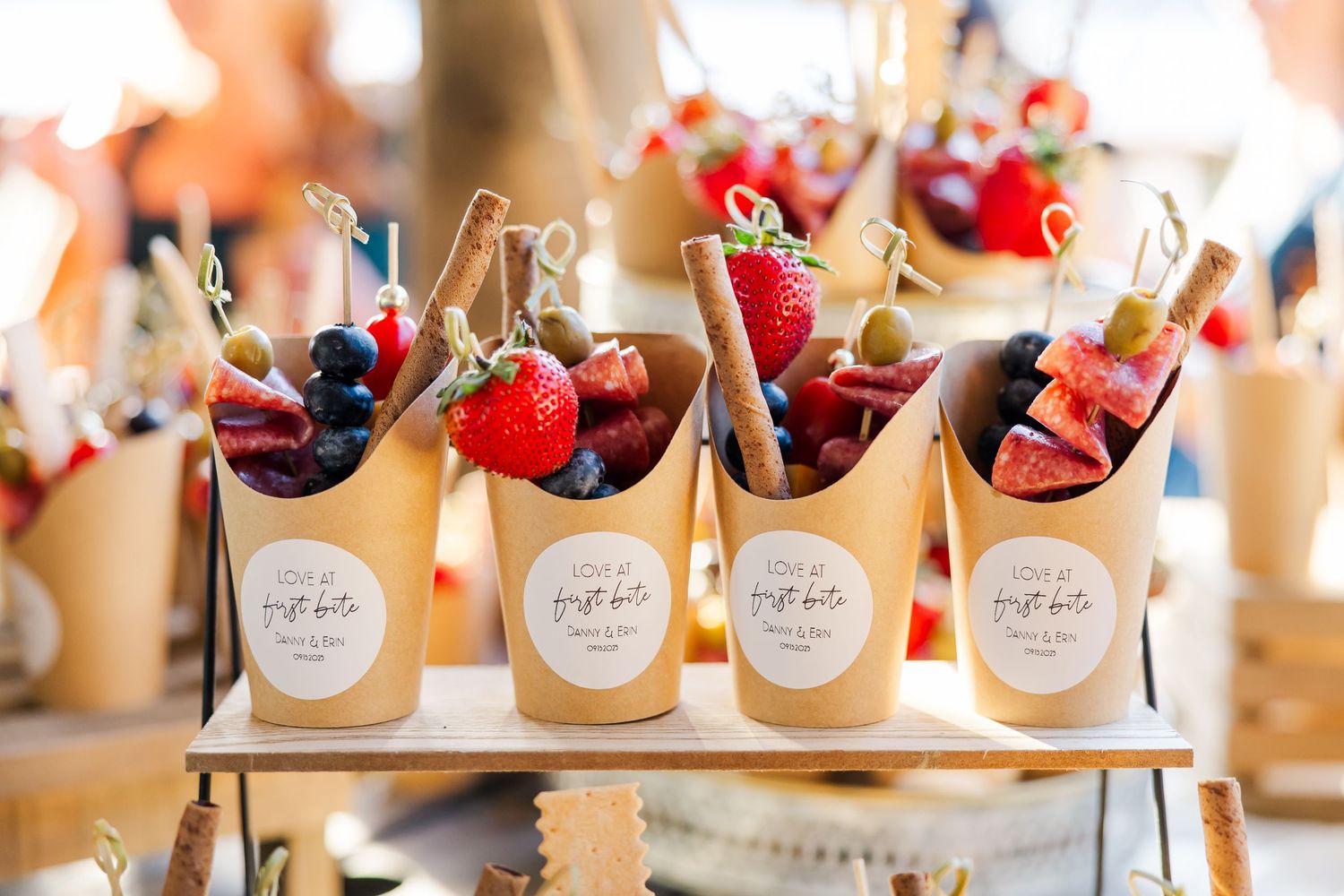 Kraft paper cones filled with fresh strawberries, blueberries, and dried fruits displayed on a wooden stand at a catered event.