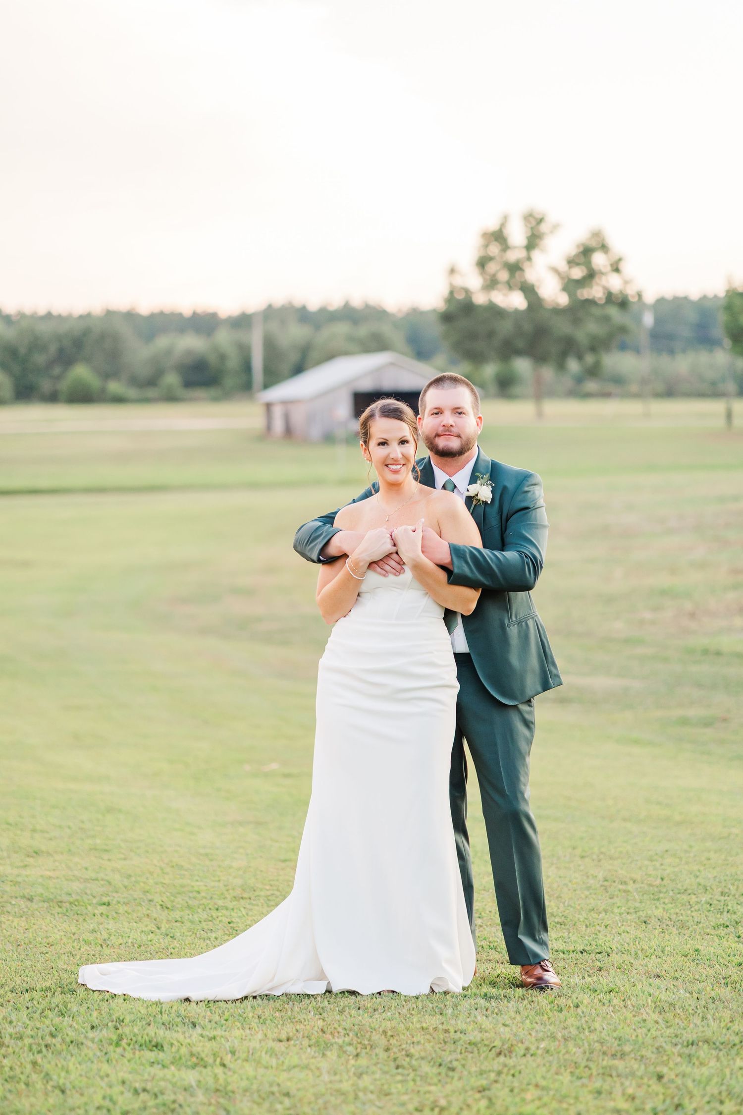 A couple dances and laughs together on a grassy field during their wedding celebration.