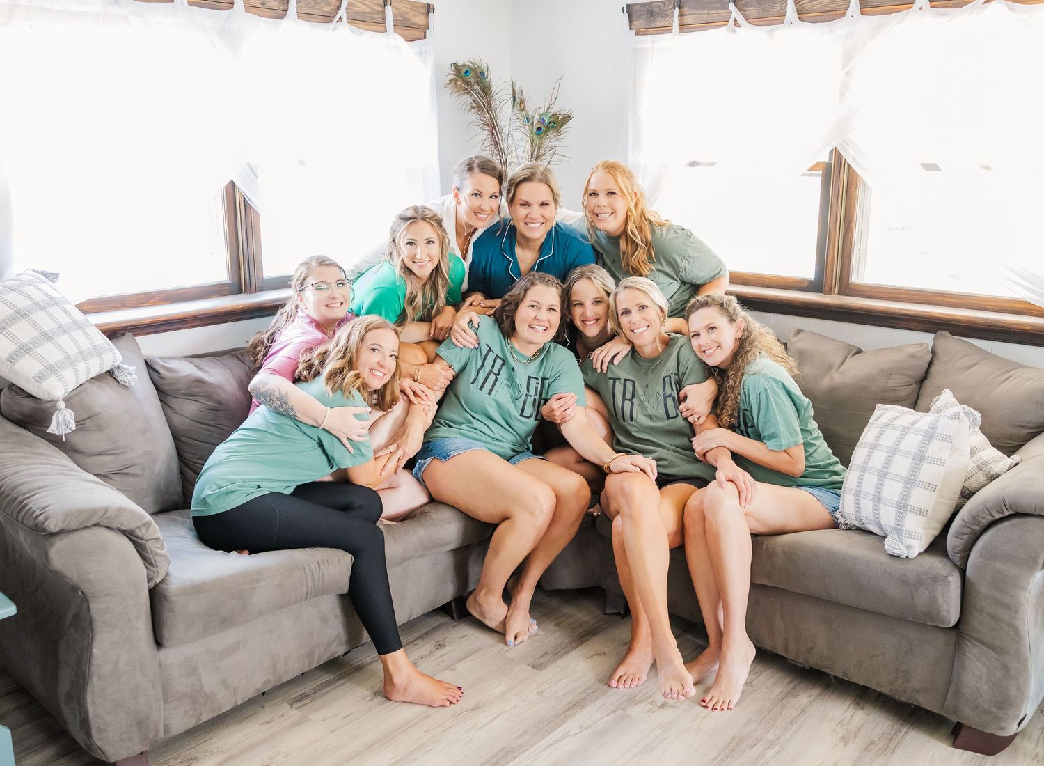 A group in matching green shirts sits together on a gray couch while smiling and laughing.