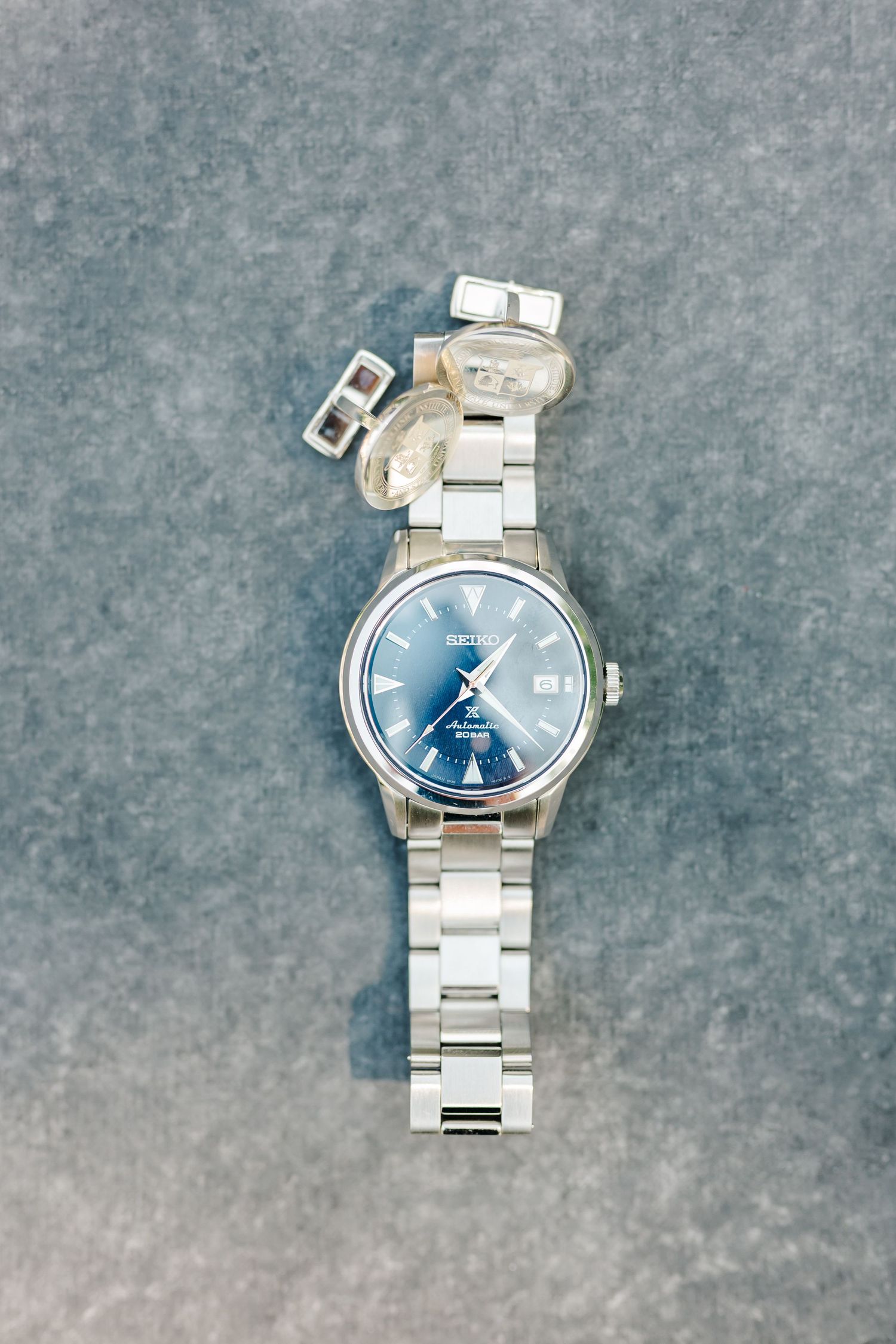 Stainless steel wristwatch with blue dial and metal bracelet shown from multiple angles on gray textured background.