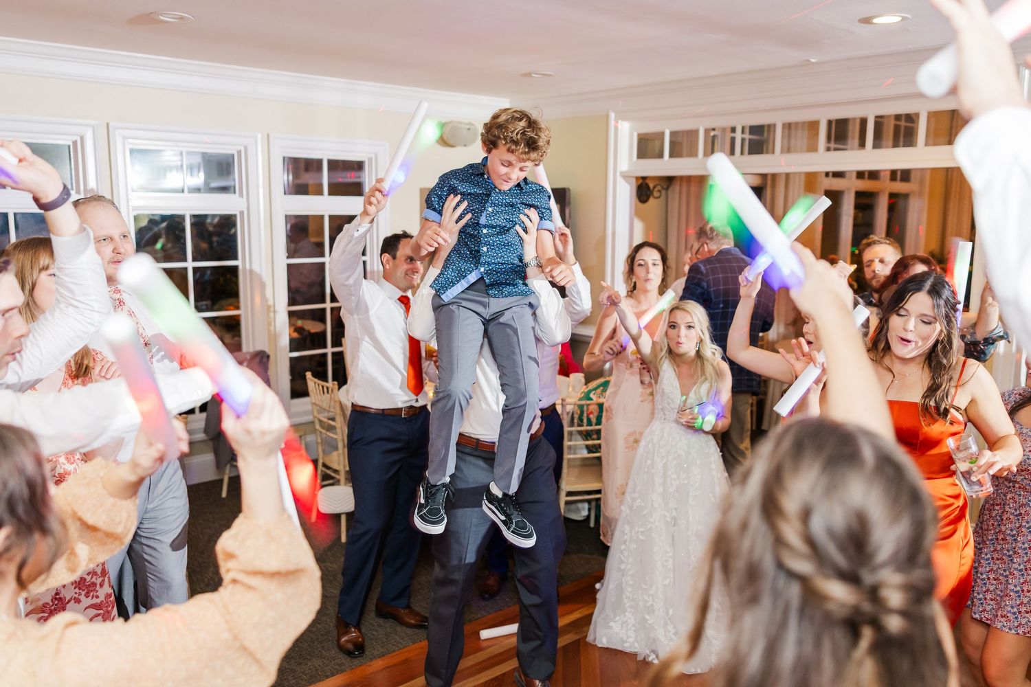 Guests enjoying themselves dancing at a lively wedding reception with colorful lights.
