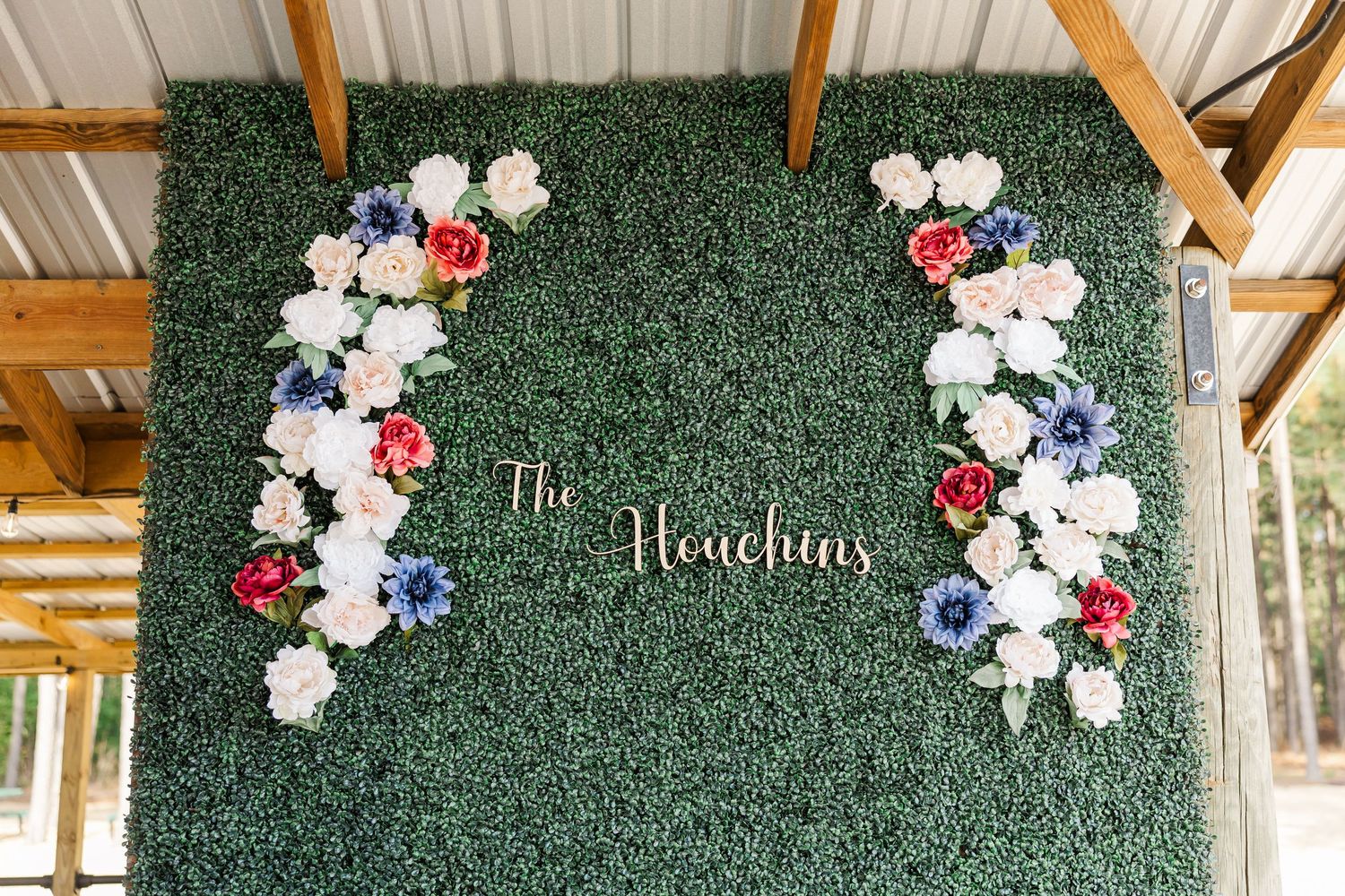 Elegant green boxwood flower wall with white, red, and blue blooms displaying The Houchins wedding sign.